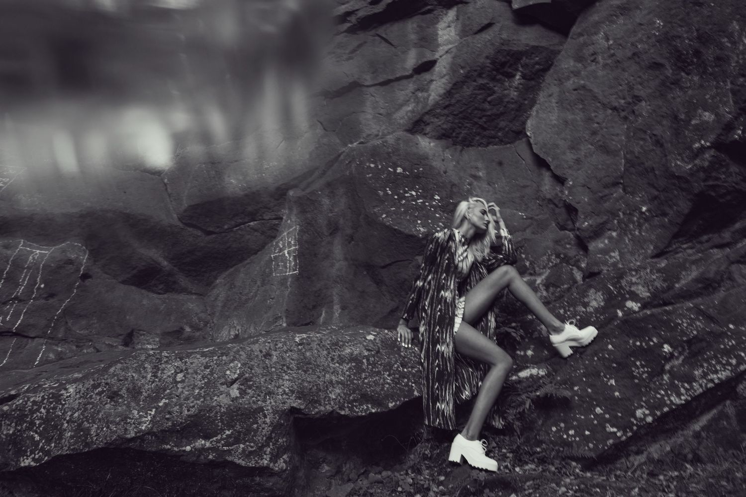 Artistic black and white photograph of a figure perched on rocky cliffs with dramatic lighting.