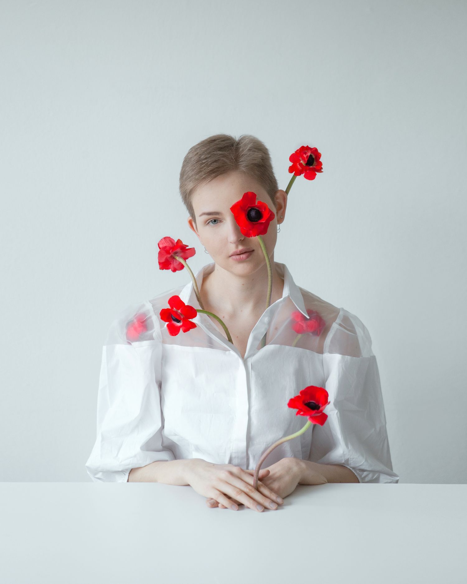Minimalist portrait series featuring vibrant red poppies and white shirt against pale background.