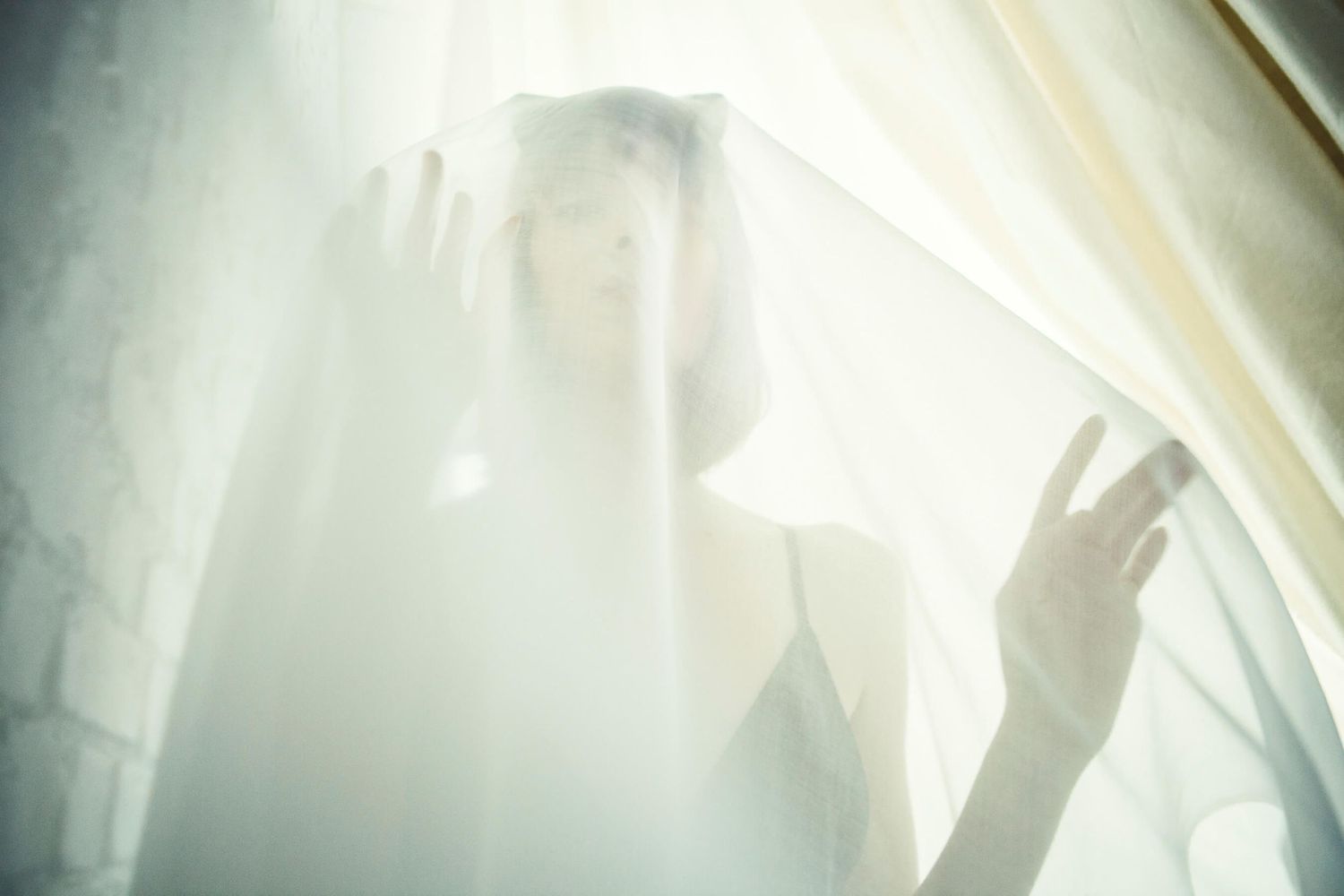 Ethereal silhouette behind sheer white fabric with dramatic lighting creating mysterious mood.