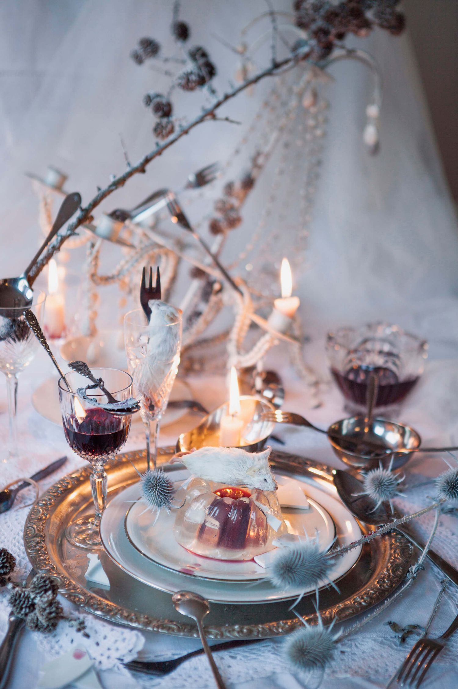 Elegant winter table setting with candles and frosted branches in cool tones.