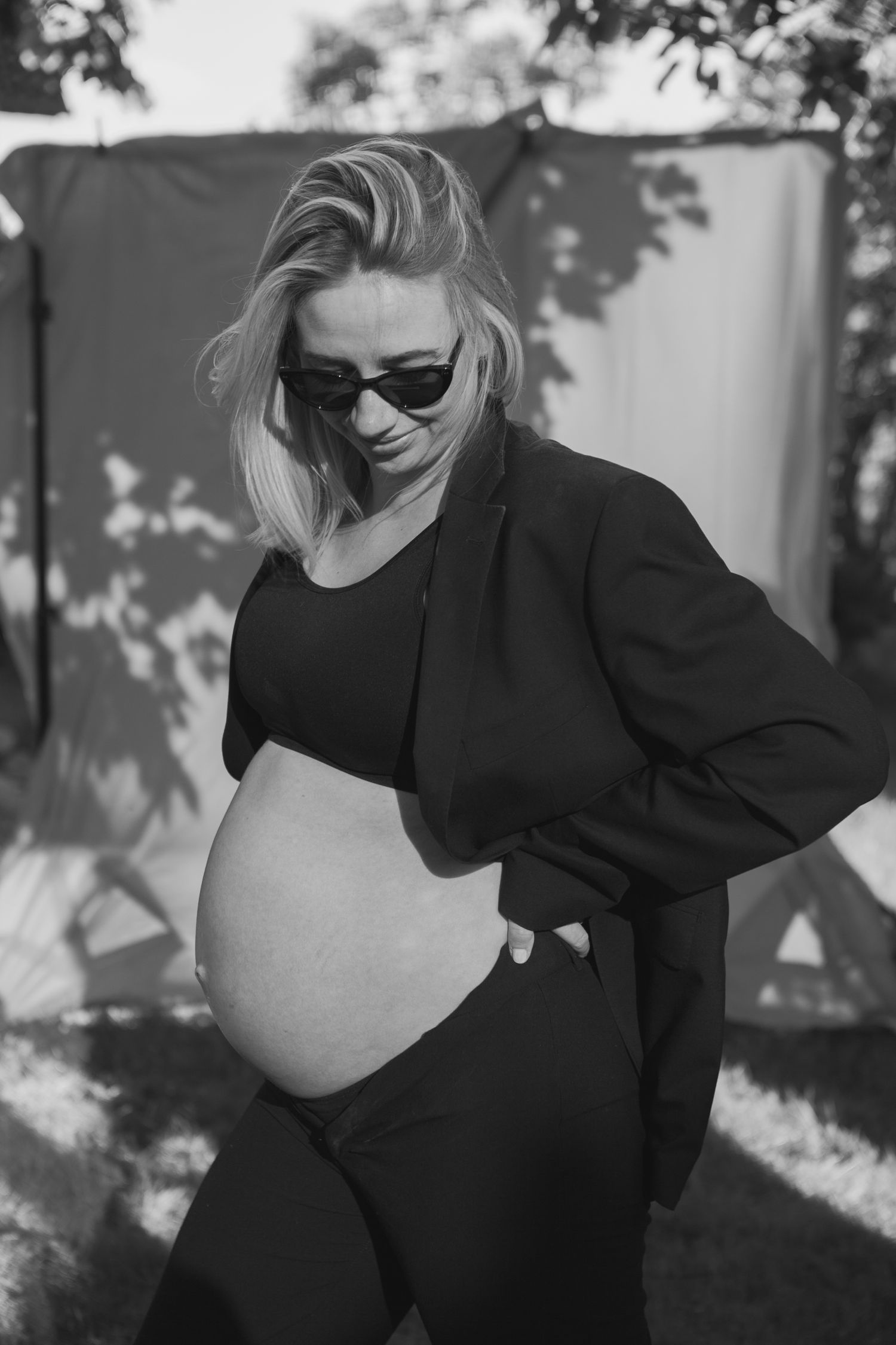 Modern maternity portrait with woman in black outfit and sunglasses against natural lighting.