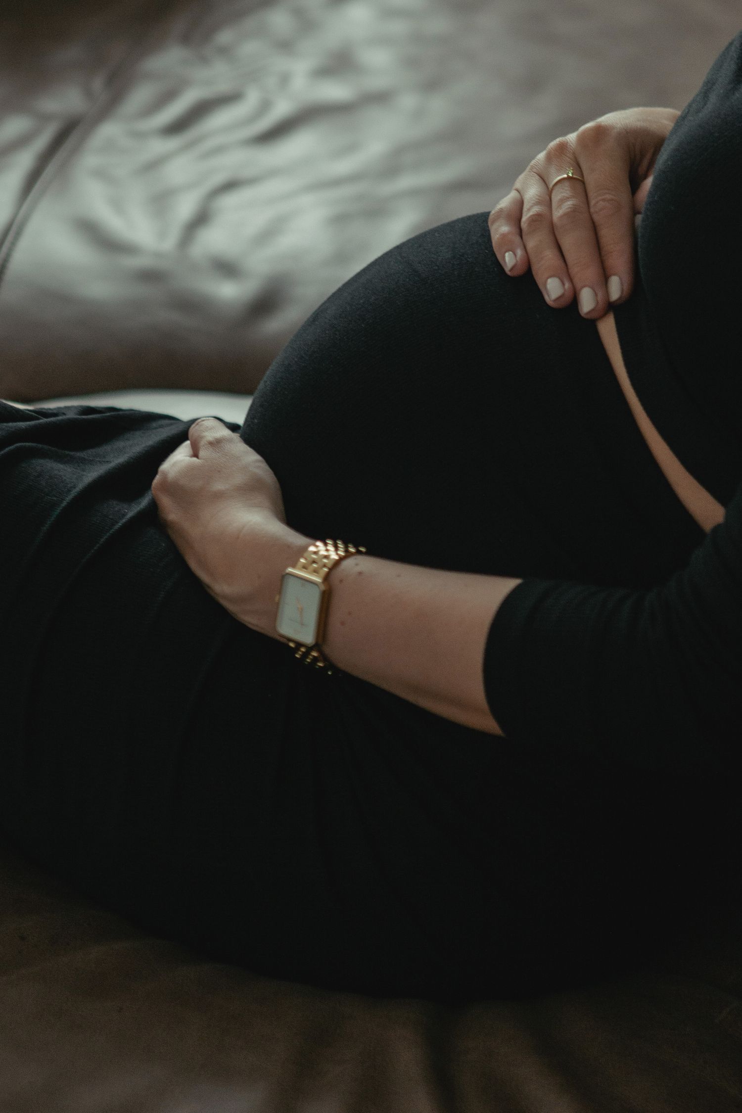 A person wearing black pants adjusts their gold watch bracelet in a moody and dramatic close-up shot.