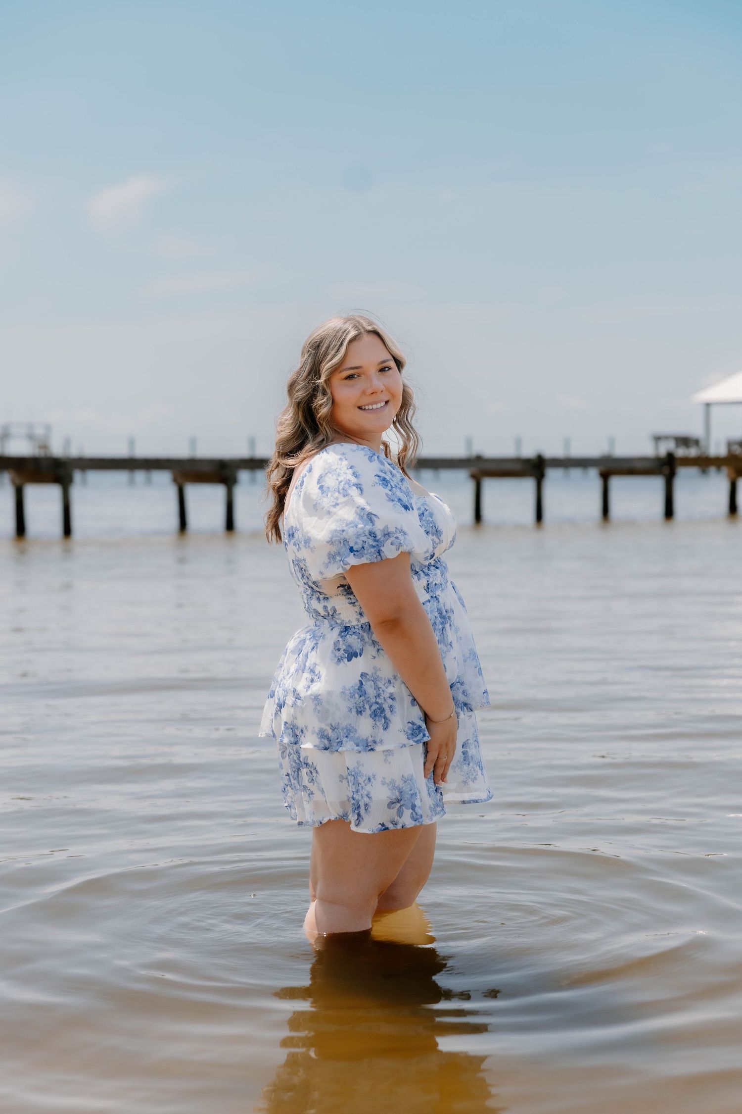 A person in a blue floral dress twirls joyfully in shallow ocean water.