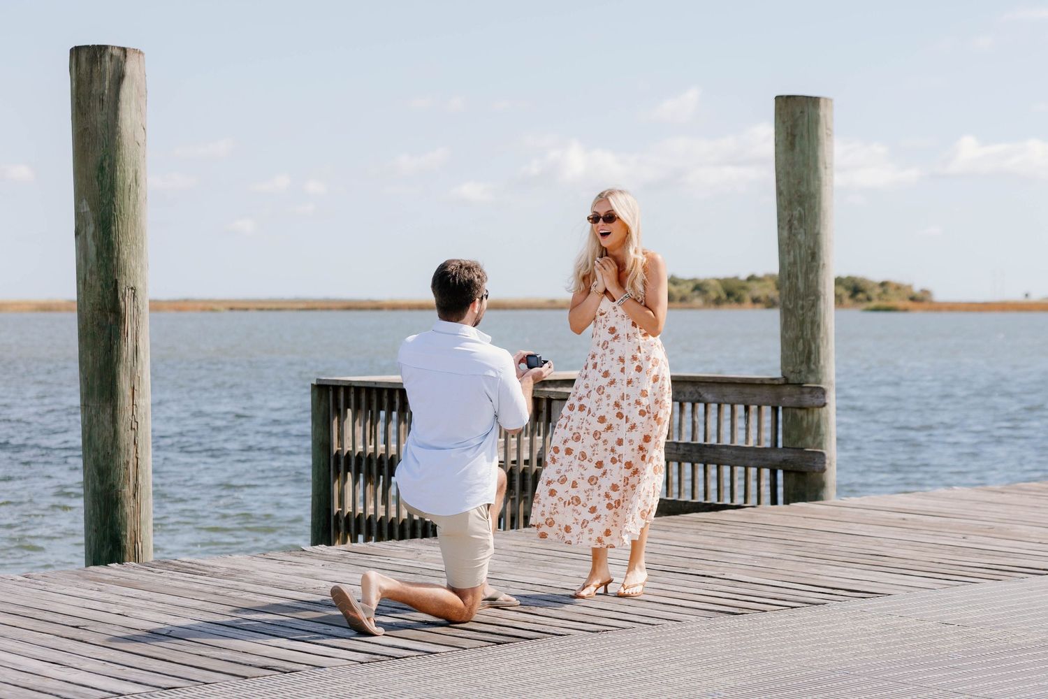 Man proposing to woman on wooden dock over water, she reacts with joy to marriage proposal.
