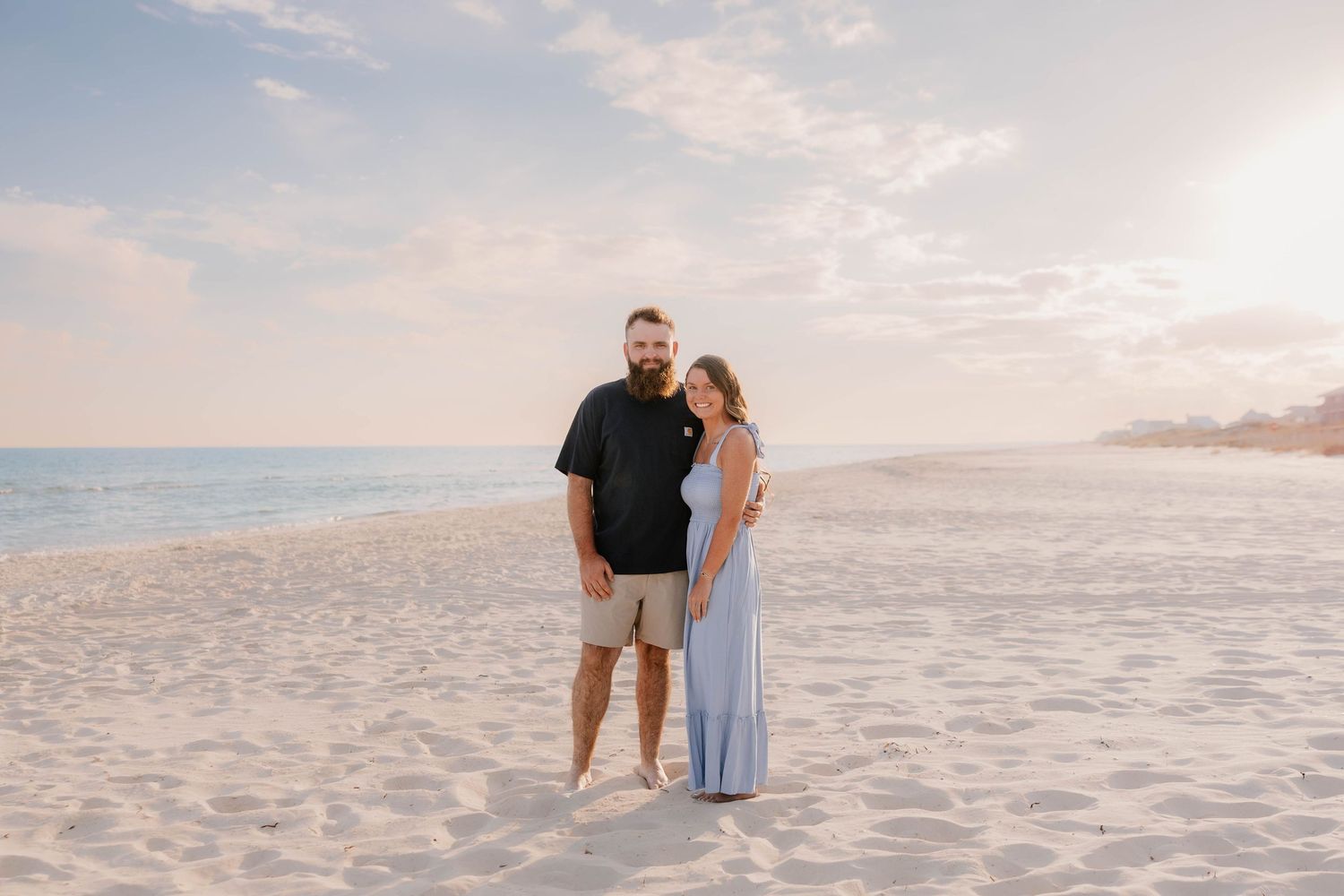 A couple walks hand in hand along a pristine white sandy beach at sunset with ocean waves in the background.
