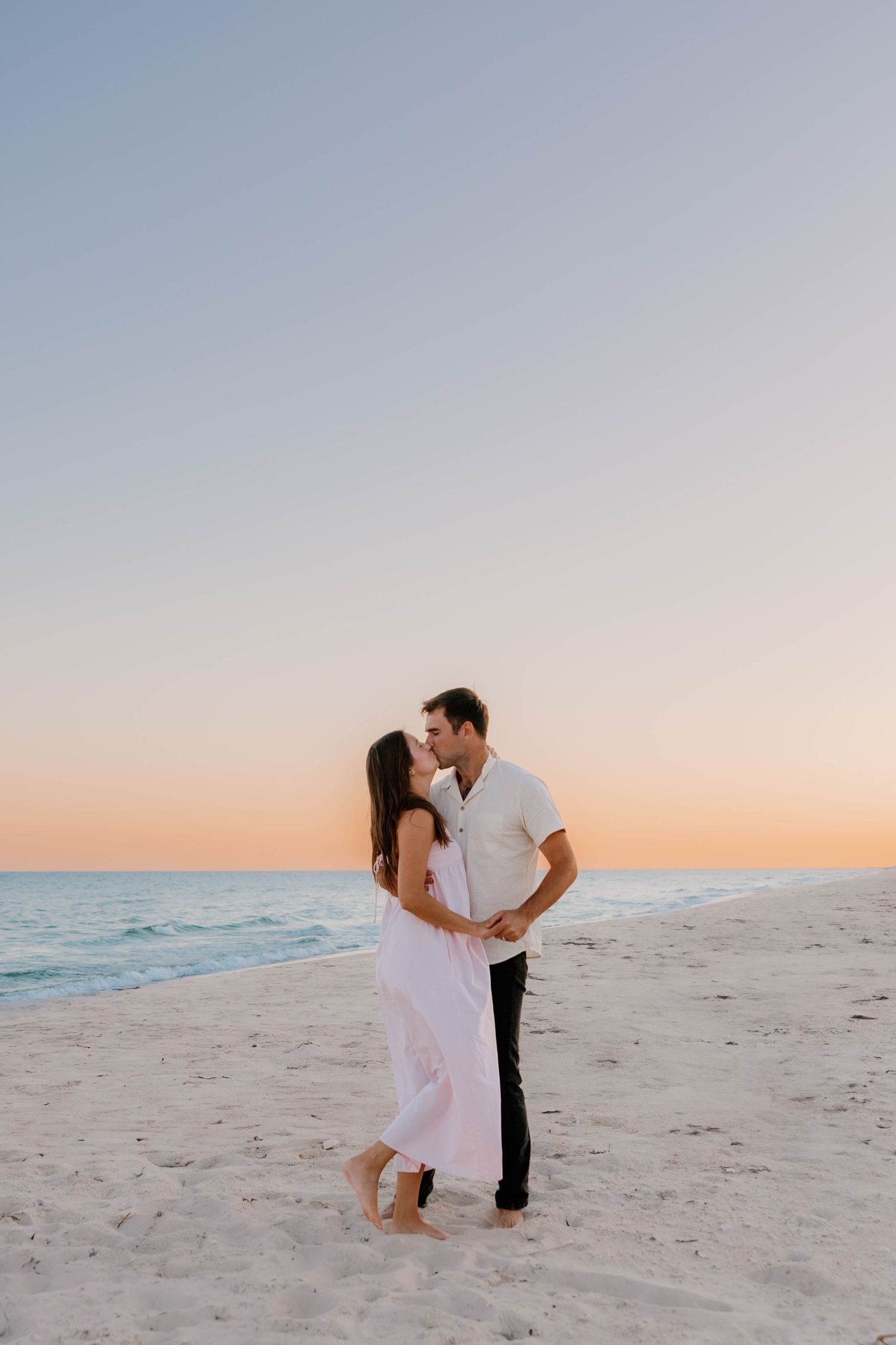 A couple shares romantic moments on a sandy beach at sunset in a series of connected photos.