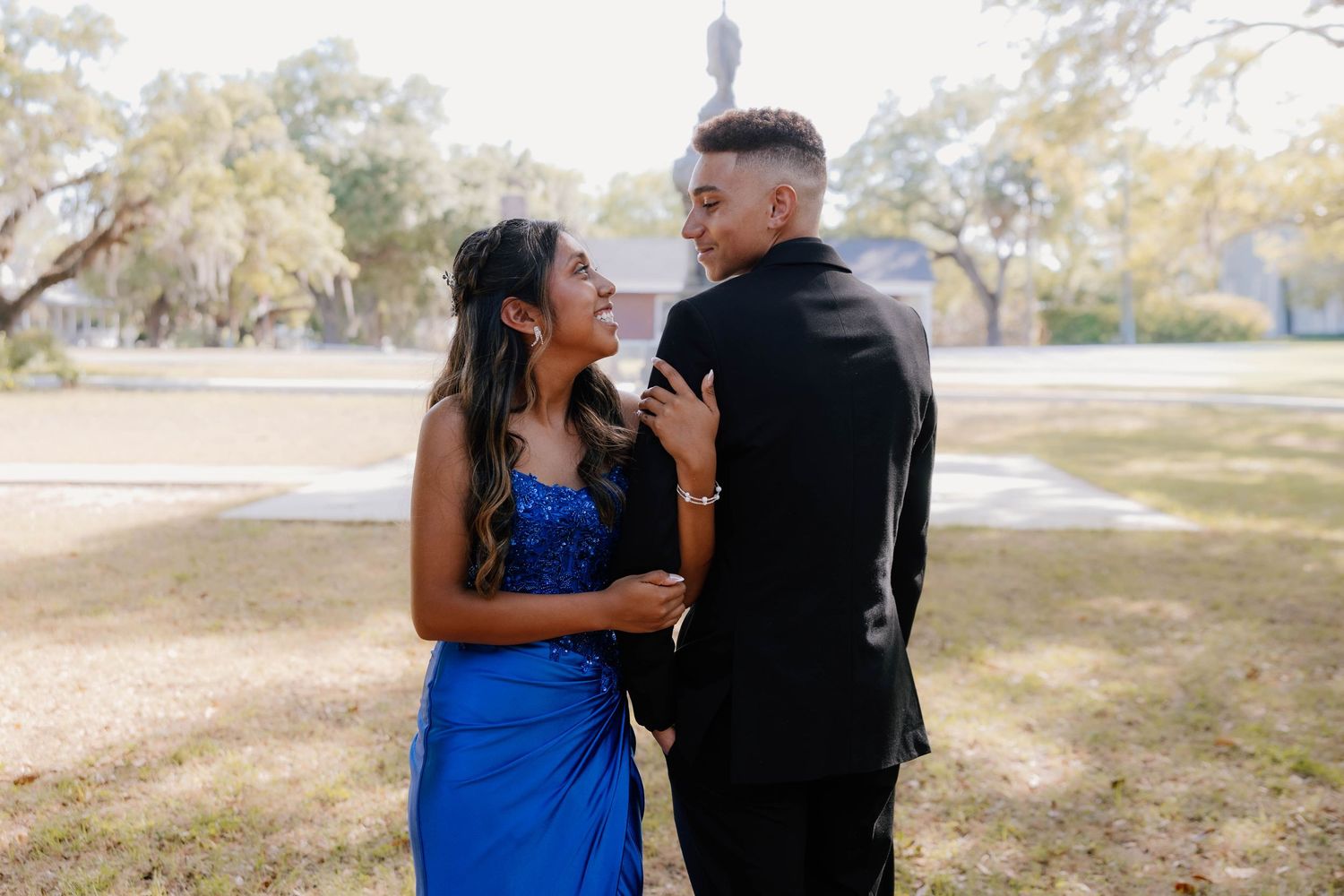 A couple in formal wear, woman in blue gown and man in black suit, share a joyful moment outdoors at prom.