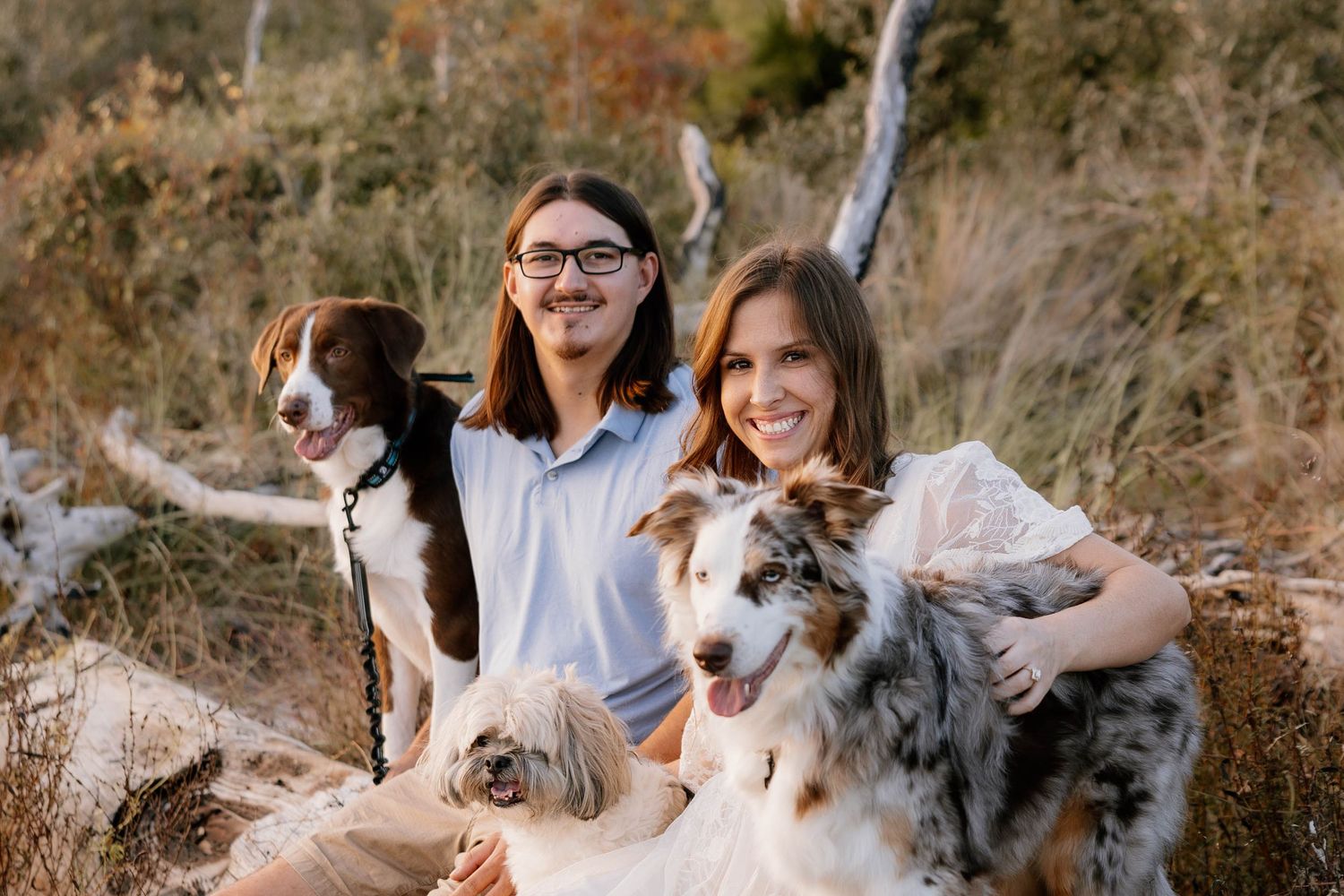 A group enjoys a sunny autumn day outdoors with their Australian Shepherd dogs among fallen leaves and rocks.