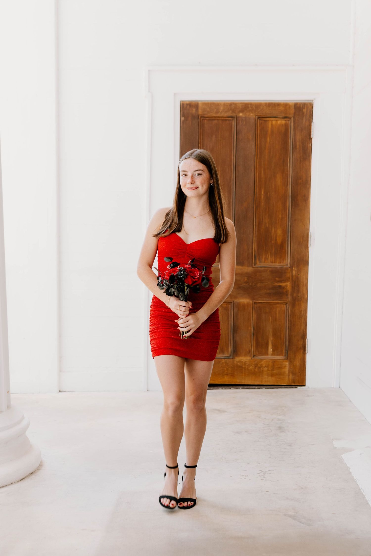A person in a red dress poses in front of wooden doors in a white studio space for a photoshoot.