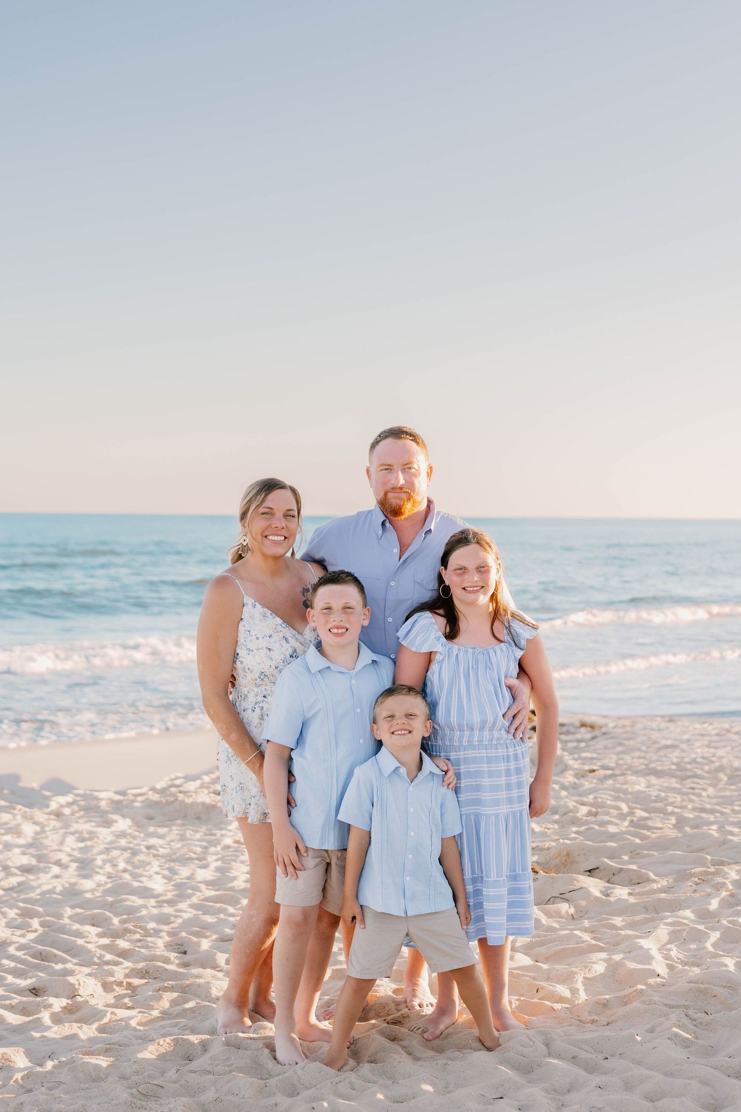 Family of five posing together on a sandy beach at sunset with ocean waves in the background.