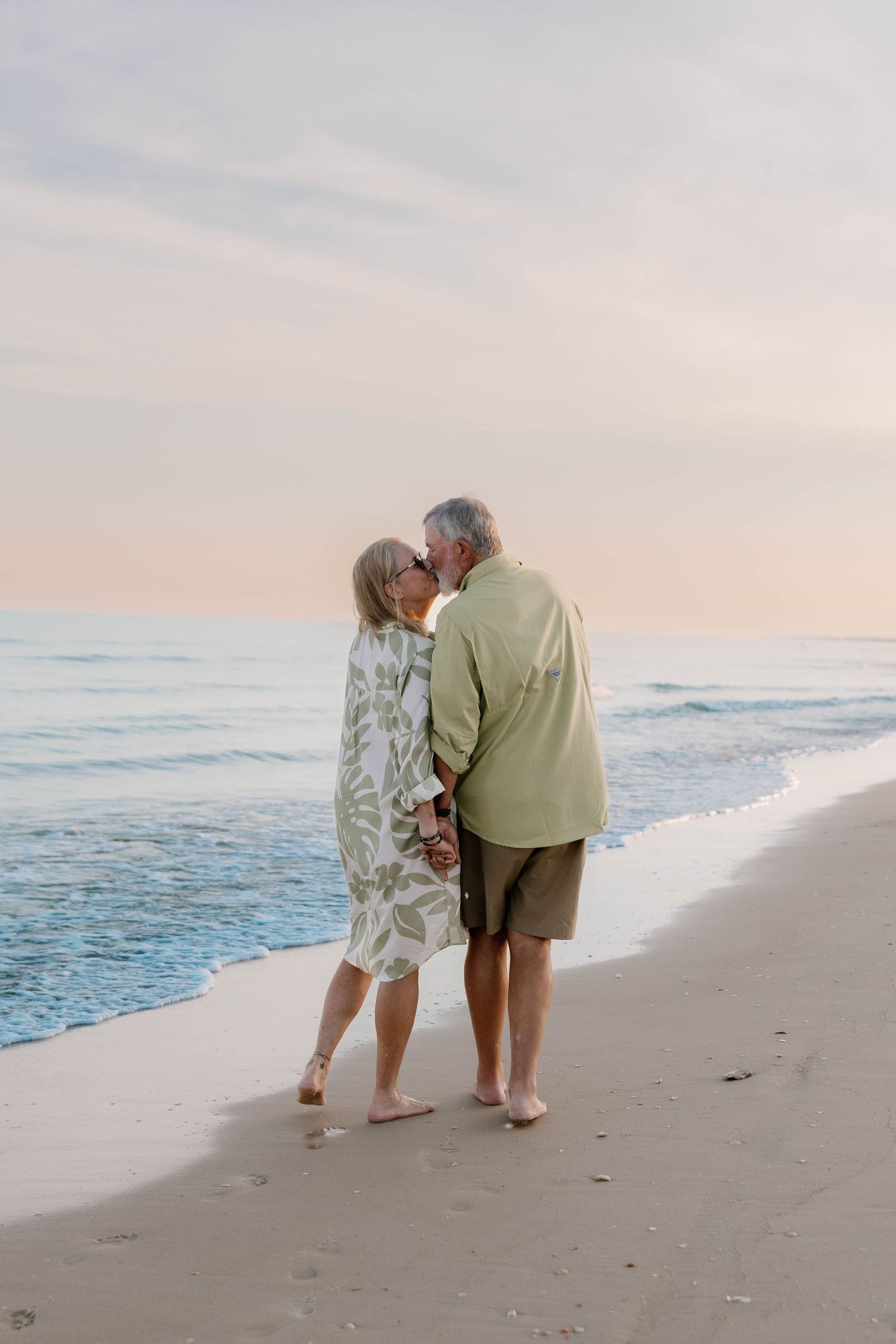 Senior couple shares intimate moment on beach at sunset.