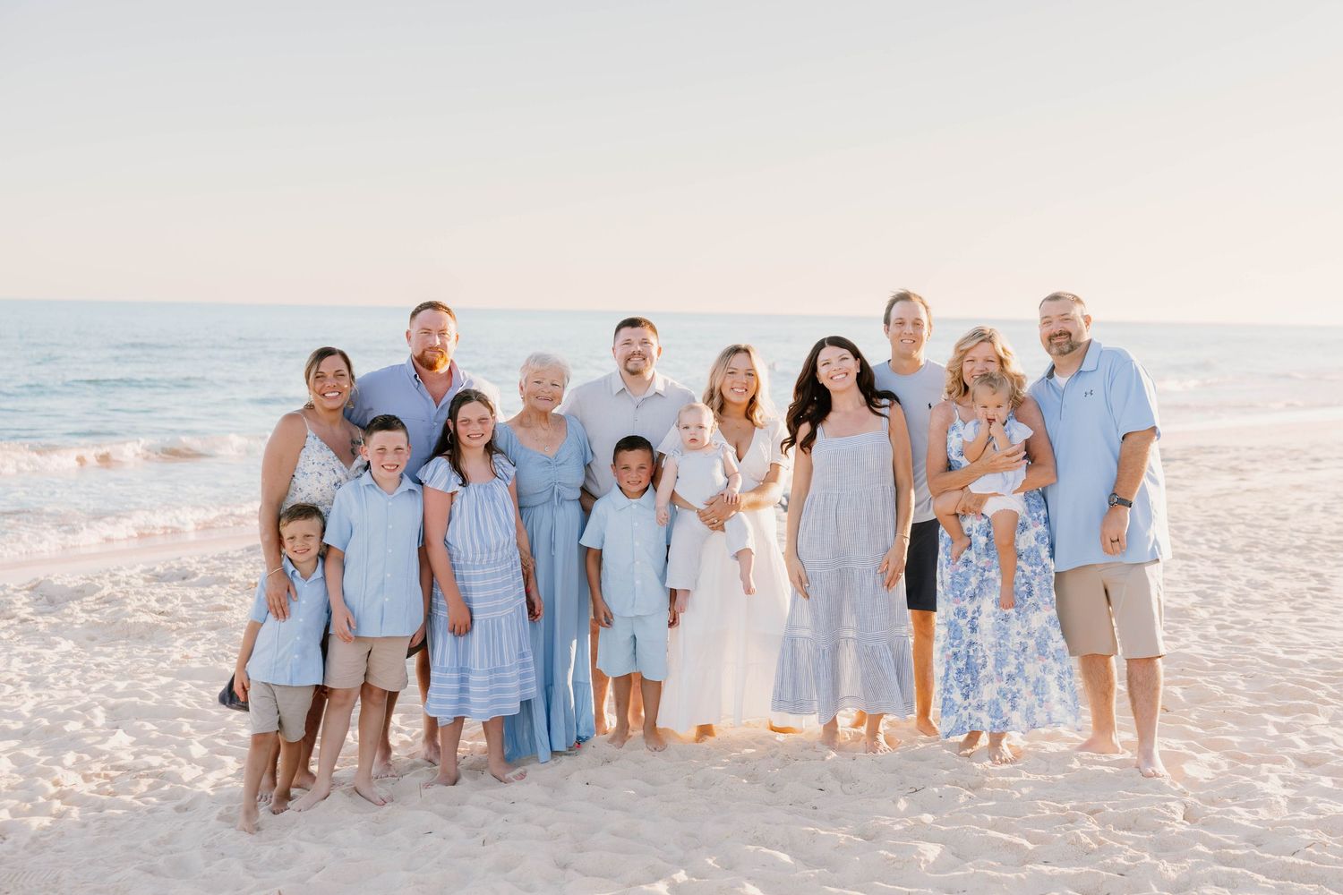 A group in coordinated blue and white outfits poses together on a sunny beach at sunset.