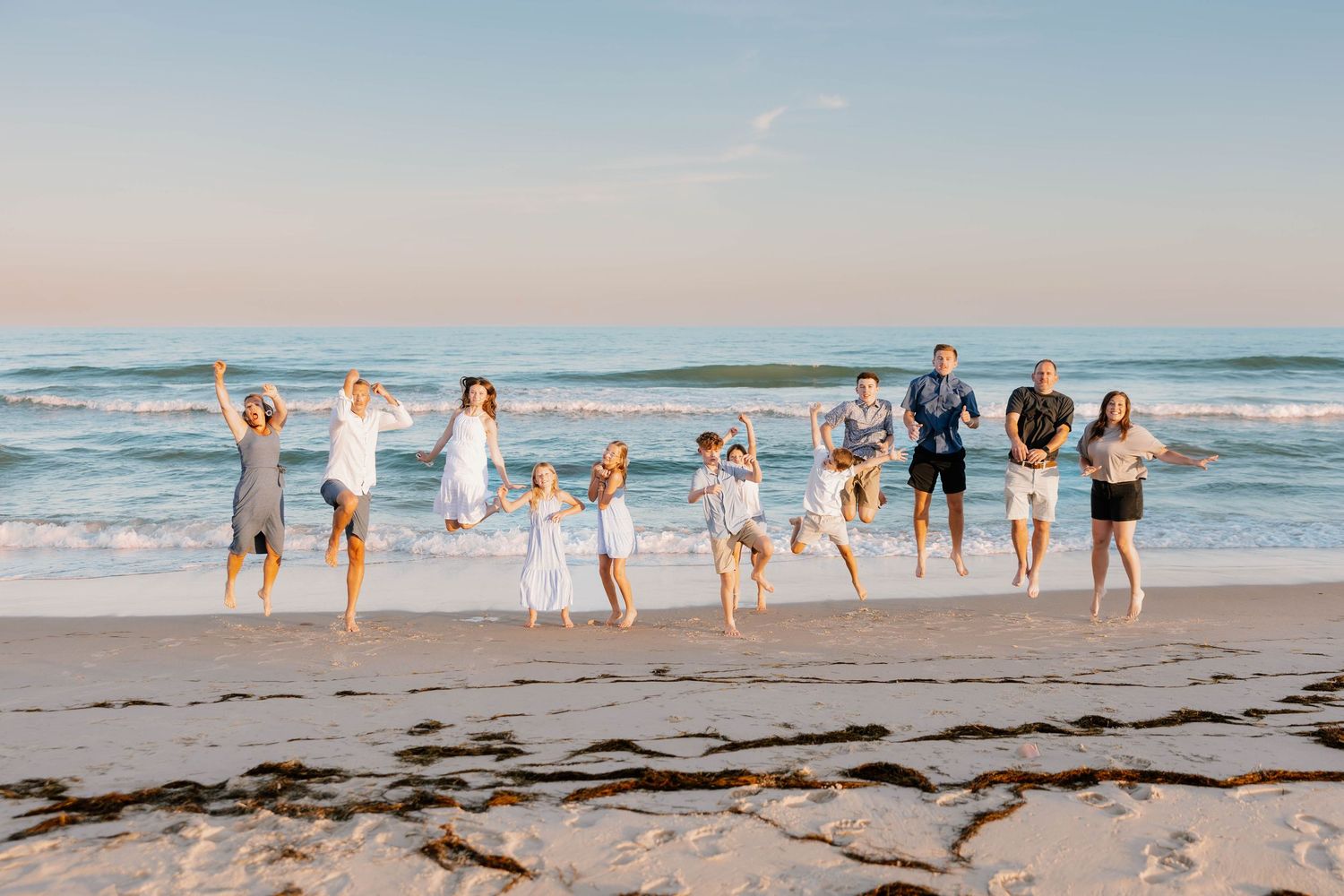 Large family jumping joyfully together on a sunny beach with ocean waves in the background.