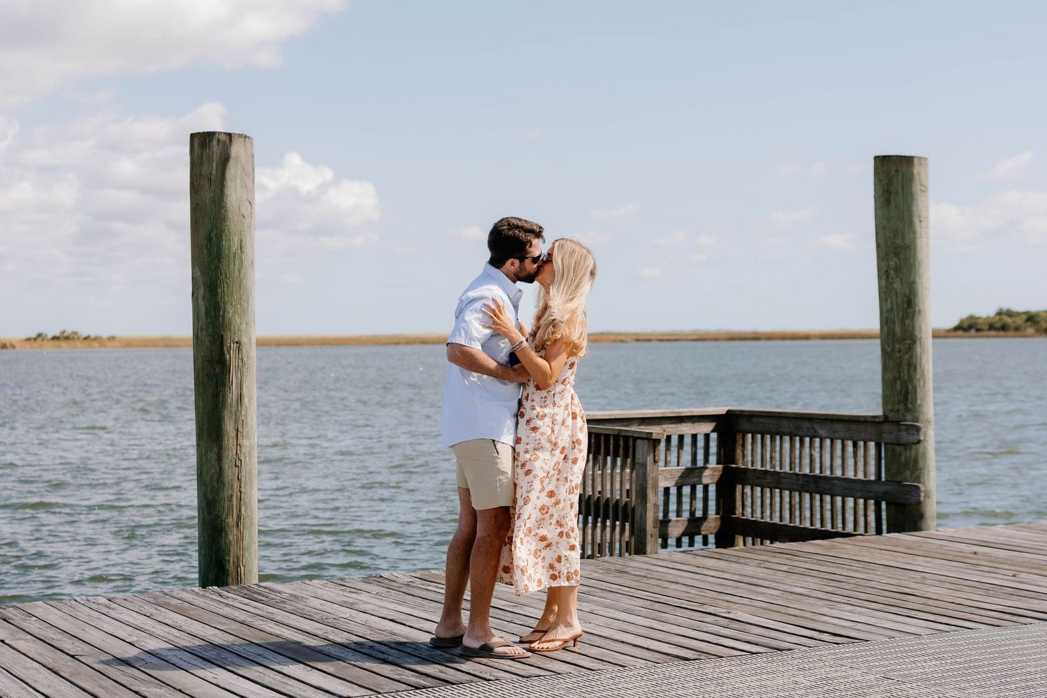 Couple sharing a romantic moment on a wooden dock by the water on a sunny day.