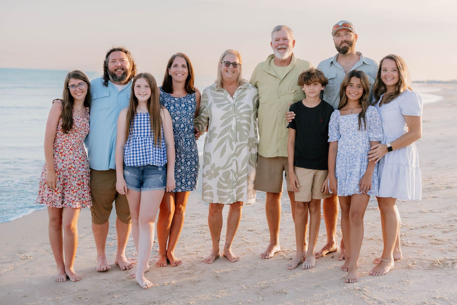 Family group poses together on sandy beach at sunset wearing coordinated casual outfits.