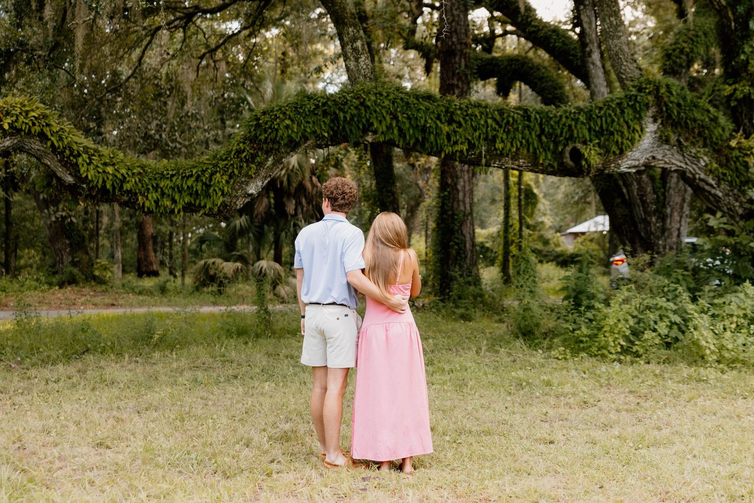 Couple standing together admiring moss-draped oak trees in a lush green forest clearing.