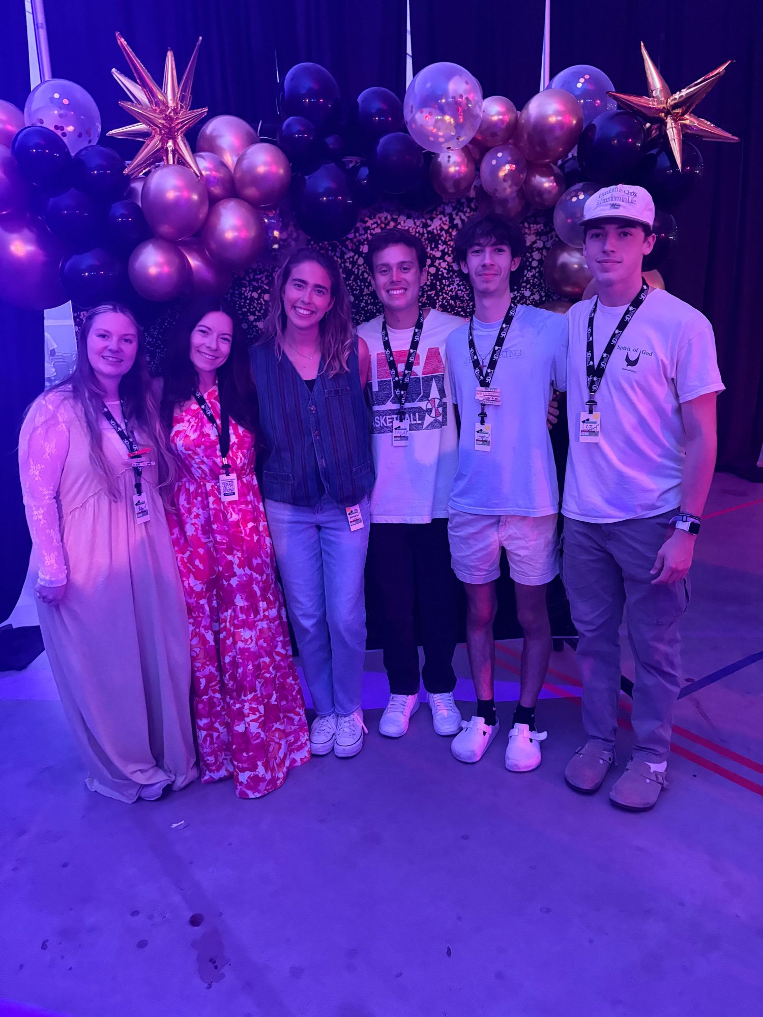 A group of people posing together under purple lighting at what appears to be a social event or gathering.