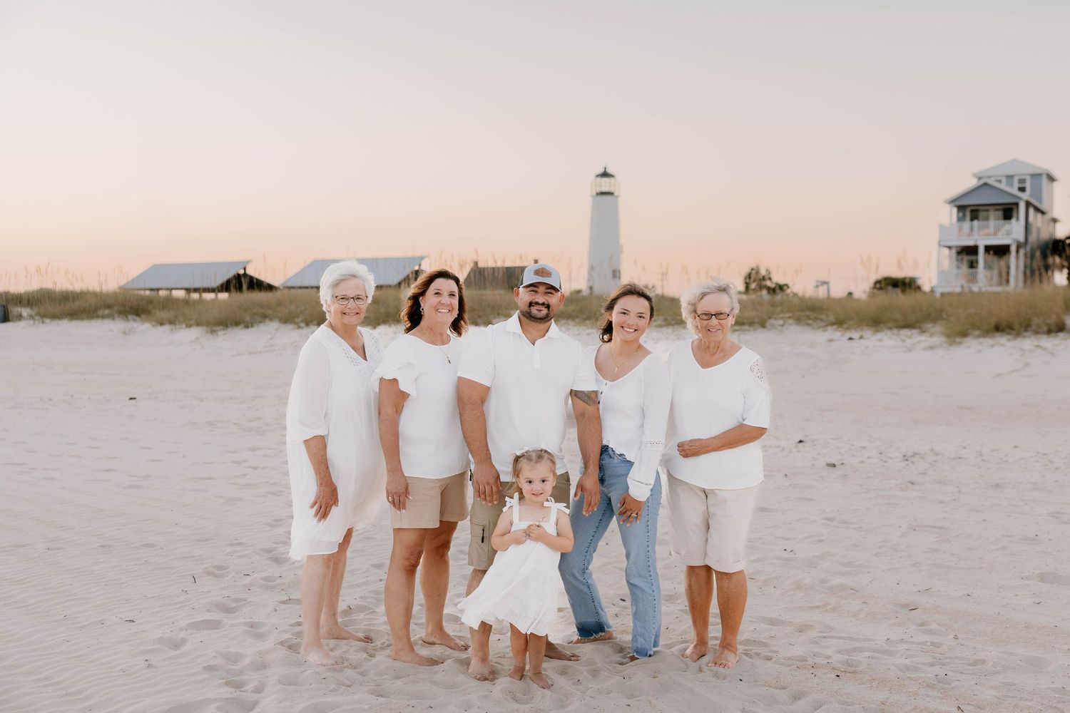 A group of people in white clothing pose together on a sandy beach during sunset.
