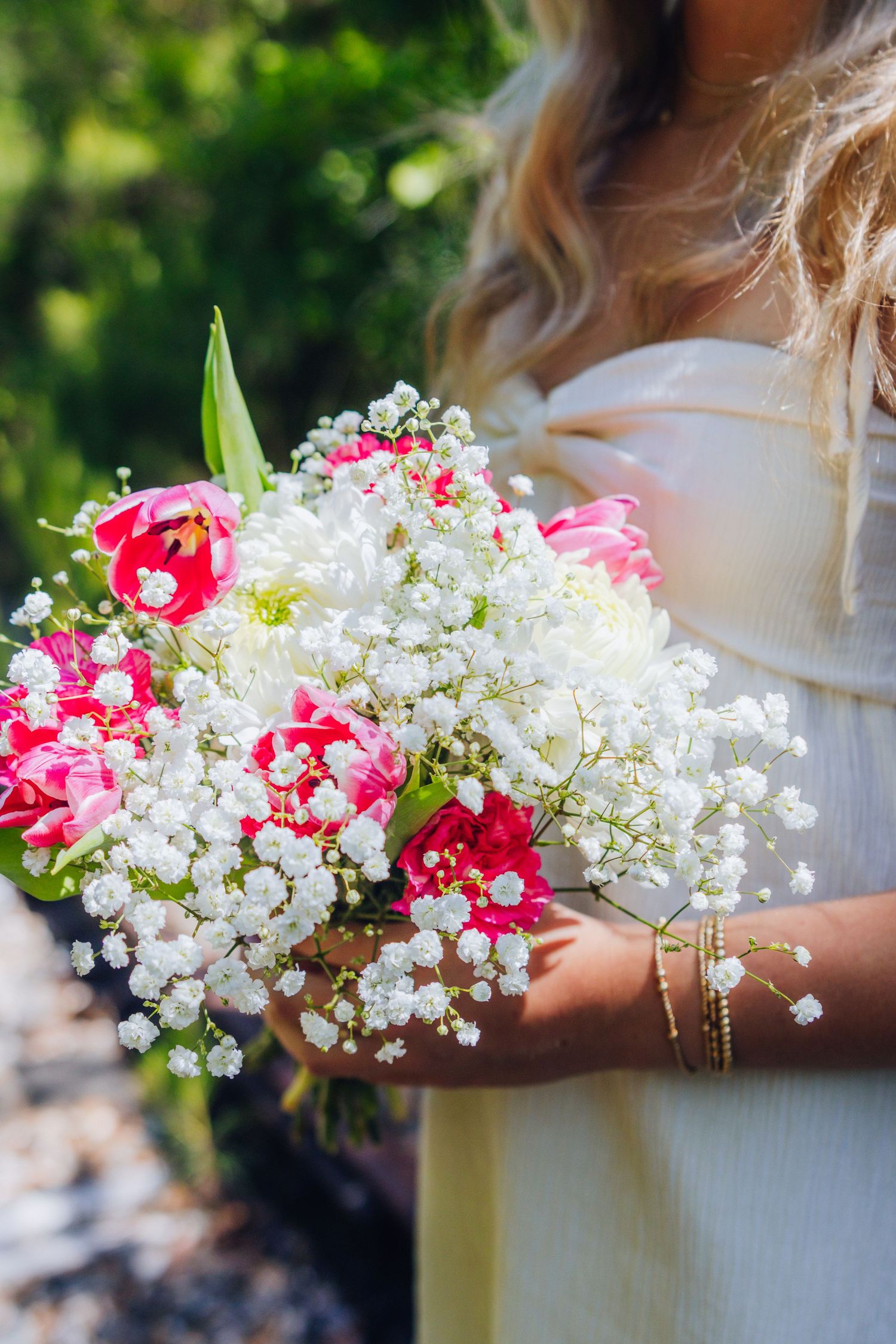 A bouquet of delicate white baby's breath flowers mixed with vibrant pink carnations held against a blurred outdoor background.