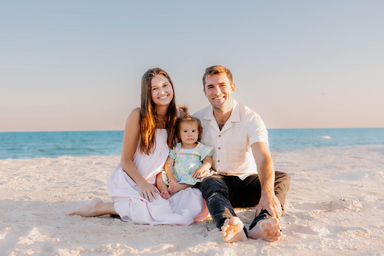 A family in white clothing poses together on a pristine white sand beach at sunset.