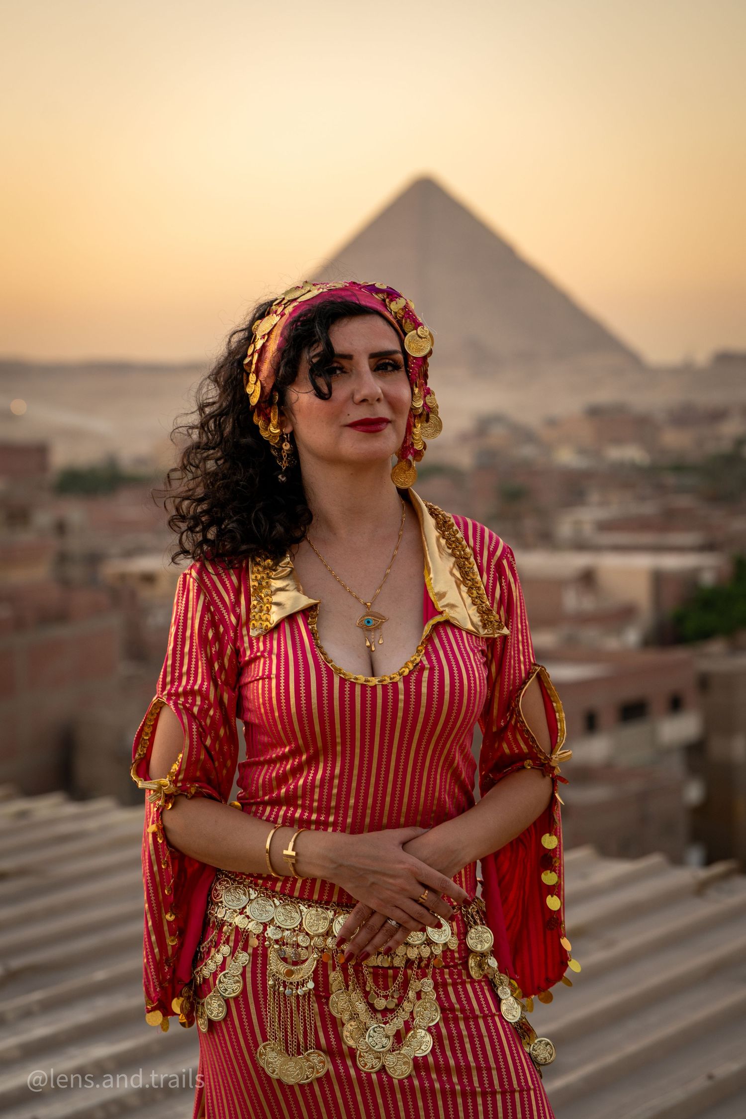 Woman in traditional red and gold Egyptian costume posing before Giza pyramid at dusk.