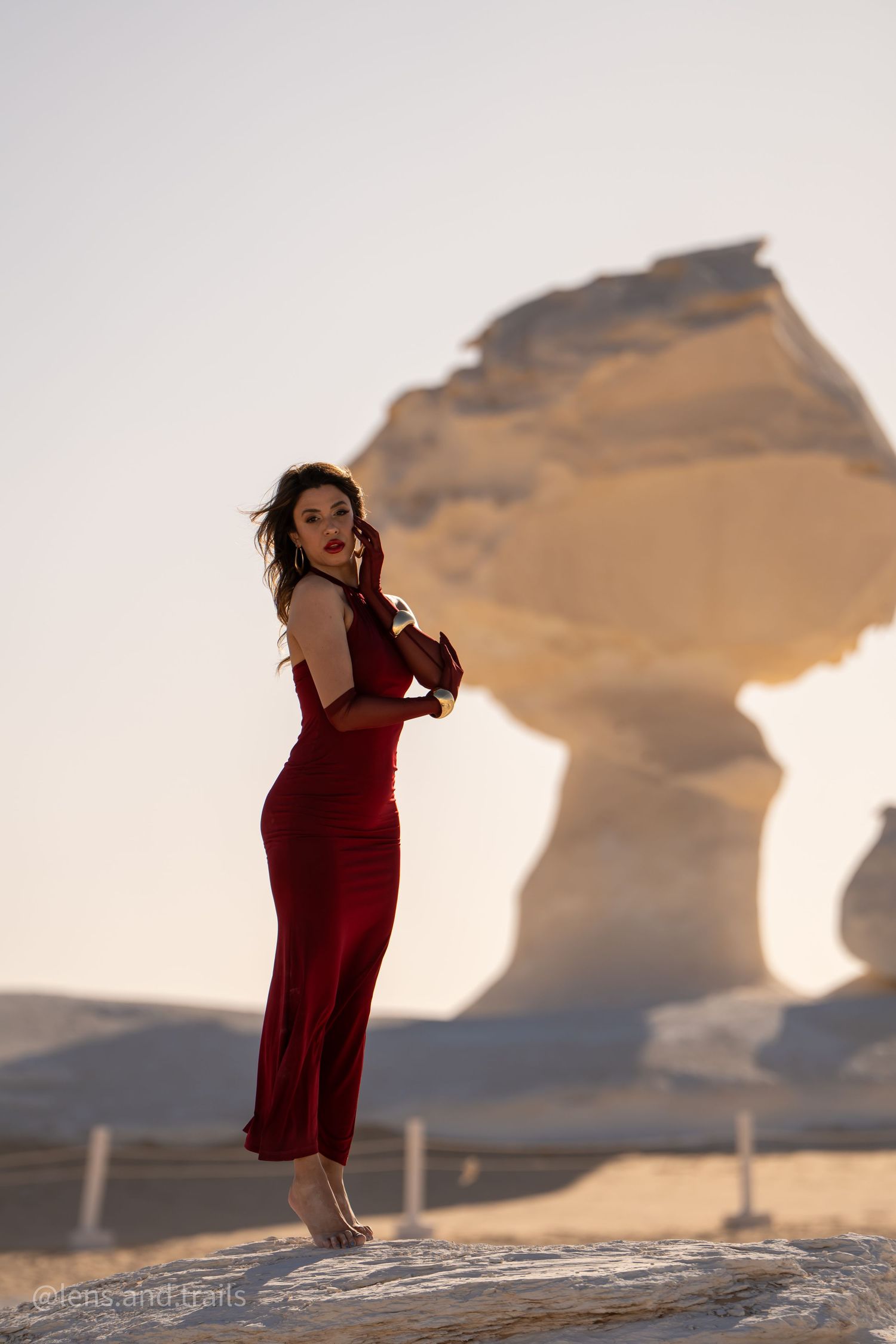 Woman in red gown stands before iconic mushroom-shaped white desert rock formation.