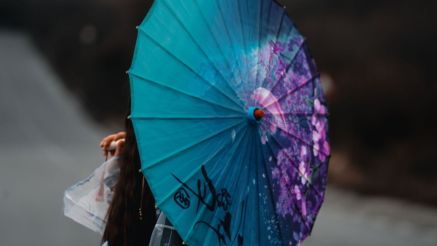 A person holds a vibrant teal Japanese oil-paper parasol with cherry blossom designs outdoors.
