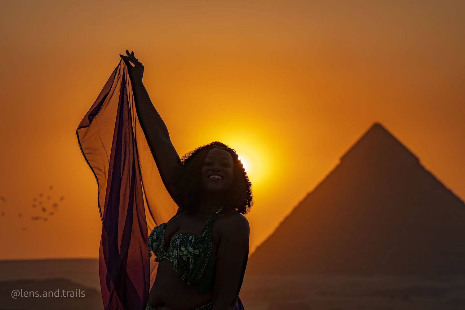 Silhouette of a joyful woman holding colorful fabric at sunset with the Egyptian pyramids in the background.