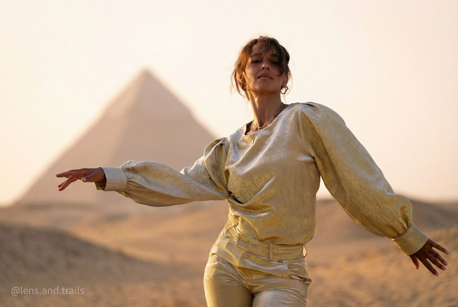 Woman in gold outfit dances expressively with the Great Pyramid of Giza at sunset behind her.