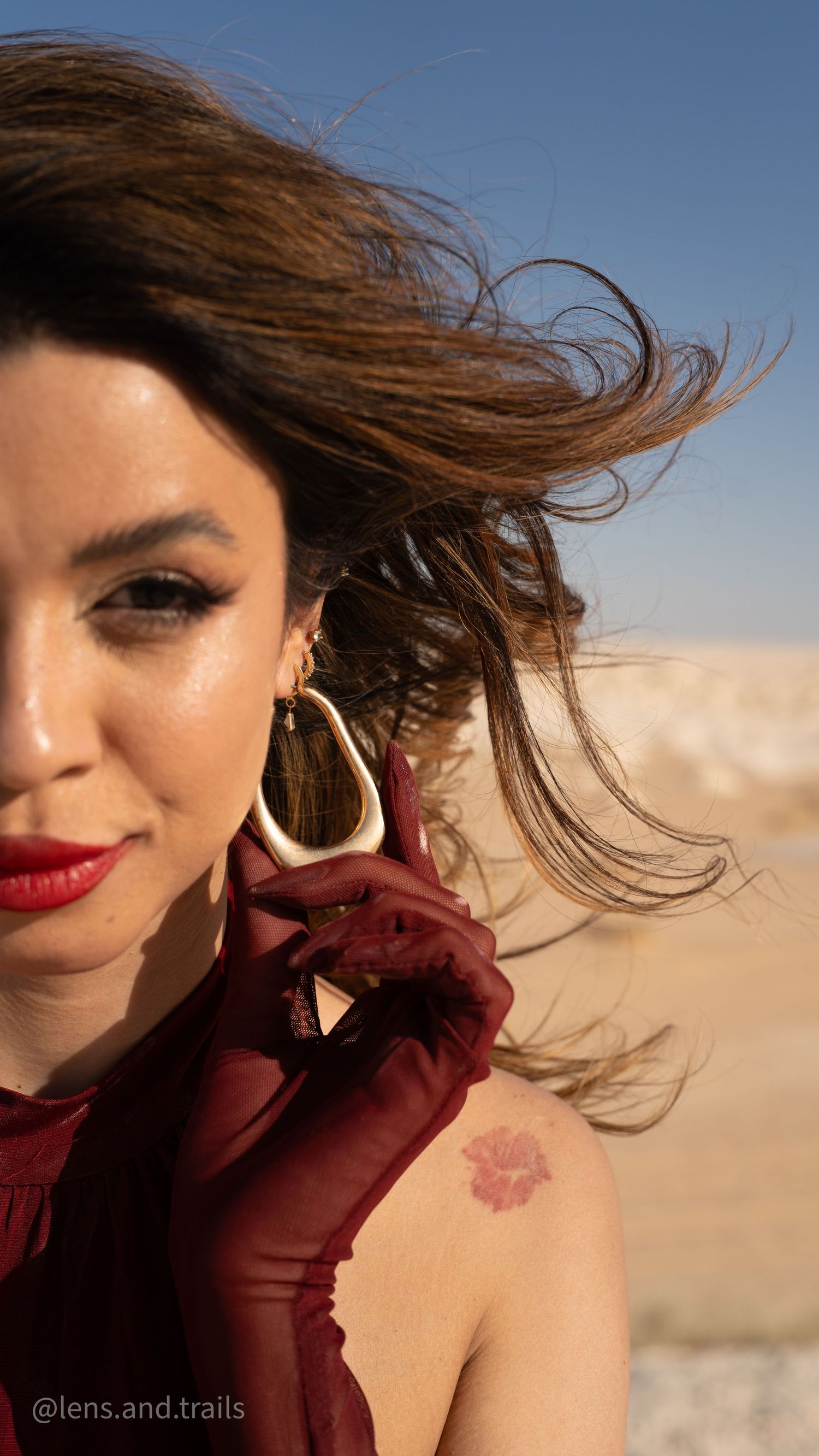 Close-up of woman with wind-blown hair wearing red gloves and statement earrings outdoors.