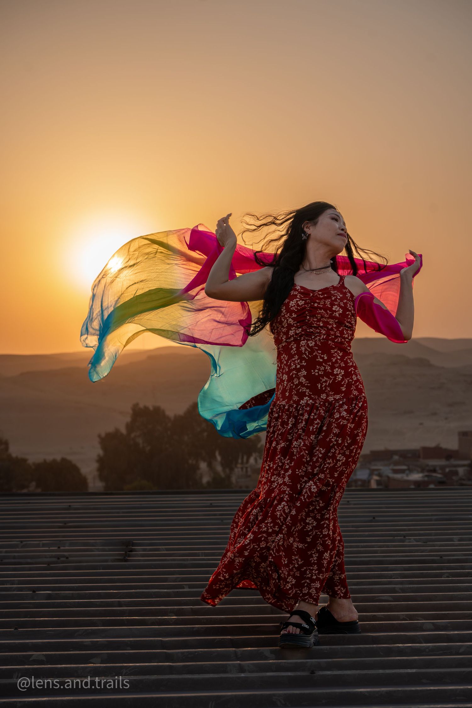 Woman in red floral dress dancing with colorful silk scarves at sunset in the desert.