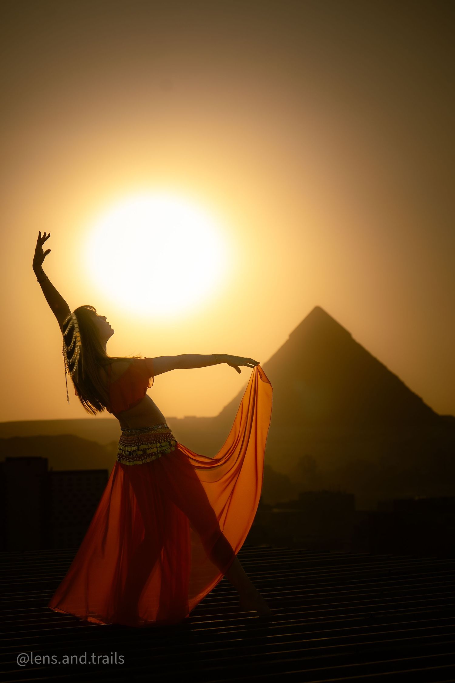 Silhouette of a belly dancer in red skirt posing gracefully with the Great Pyramid at sunset.