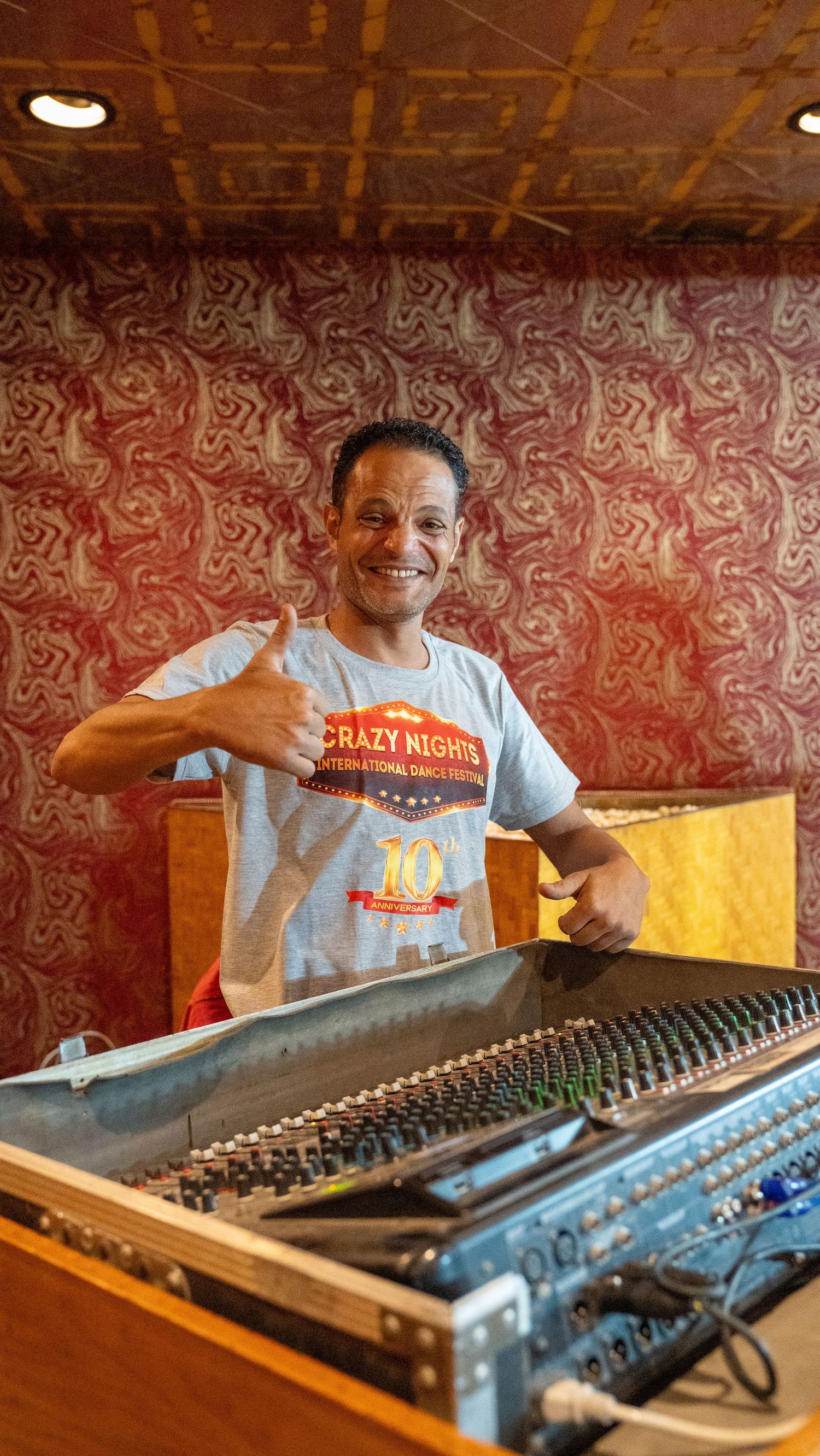Smiling sound technician gives thumbs up while operating mixing console at international dance festival.