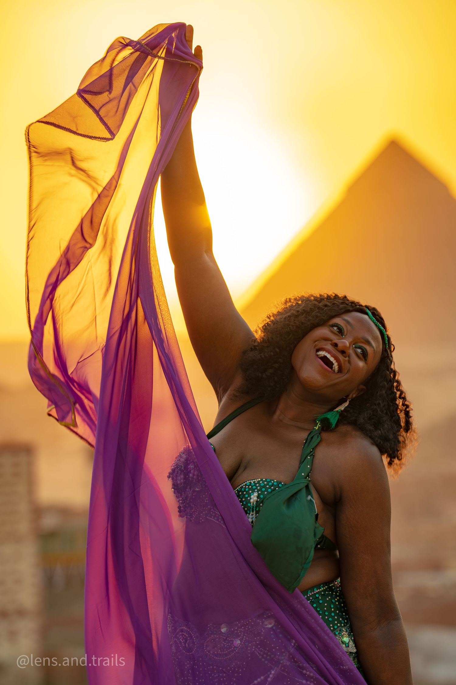Woman in green top dancing with flowing purple fabric before the pyramids at golden sunset in Egypt.