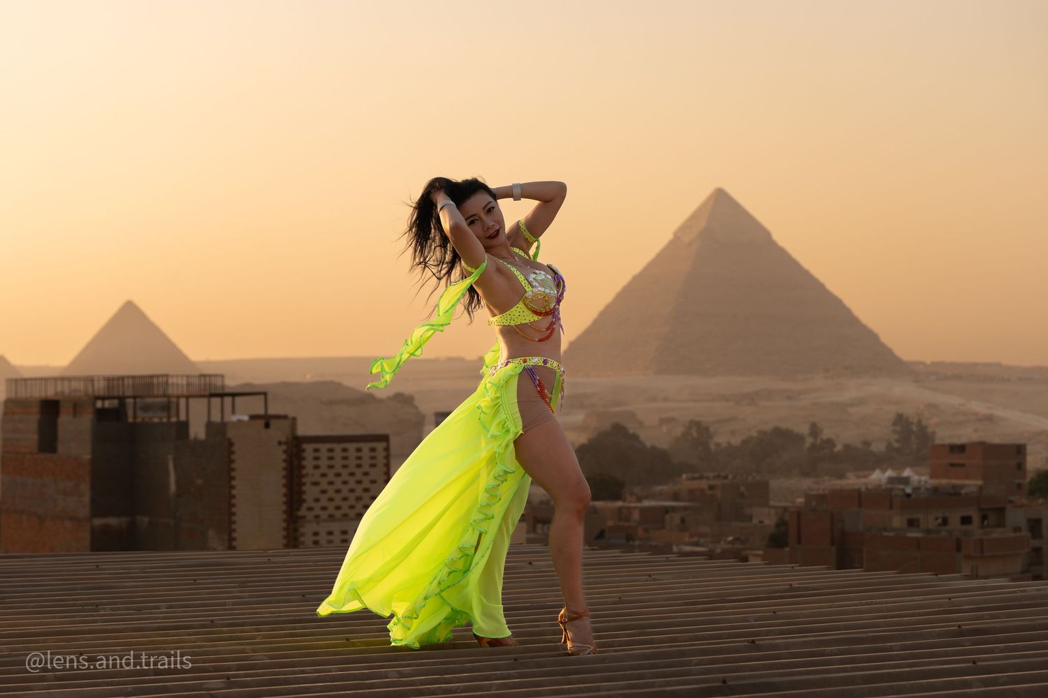Belly dancer in neon yellow costume performing with two Giza pyramids at sunset.