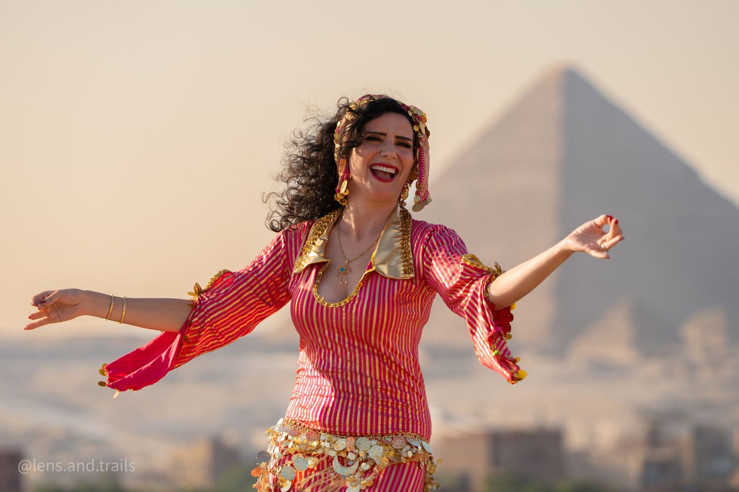 Joyful woman in red striped costume dancing with arms wide before Giza pyramid.