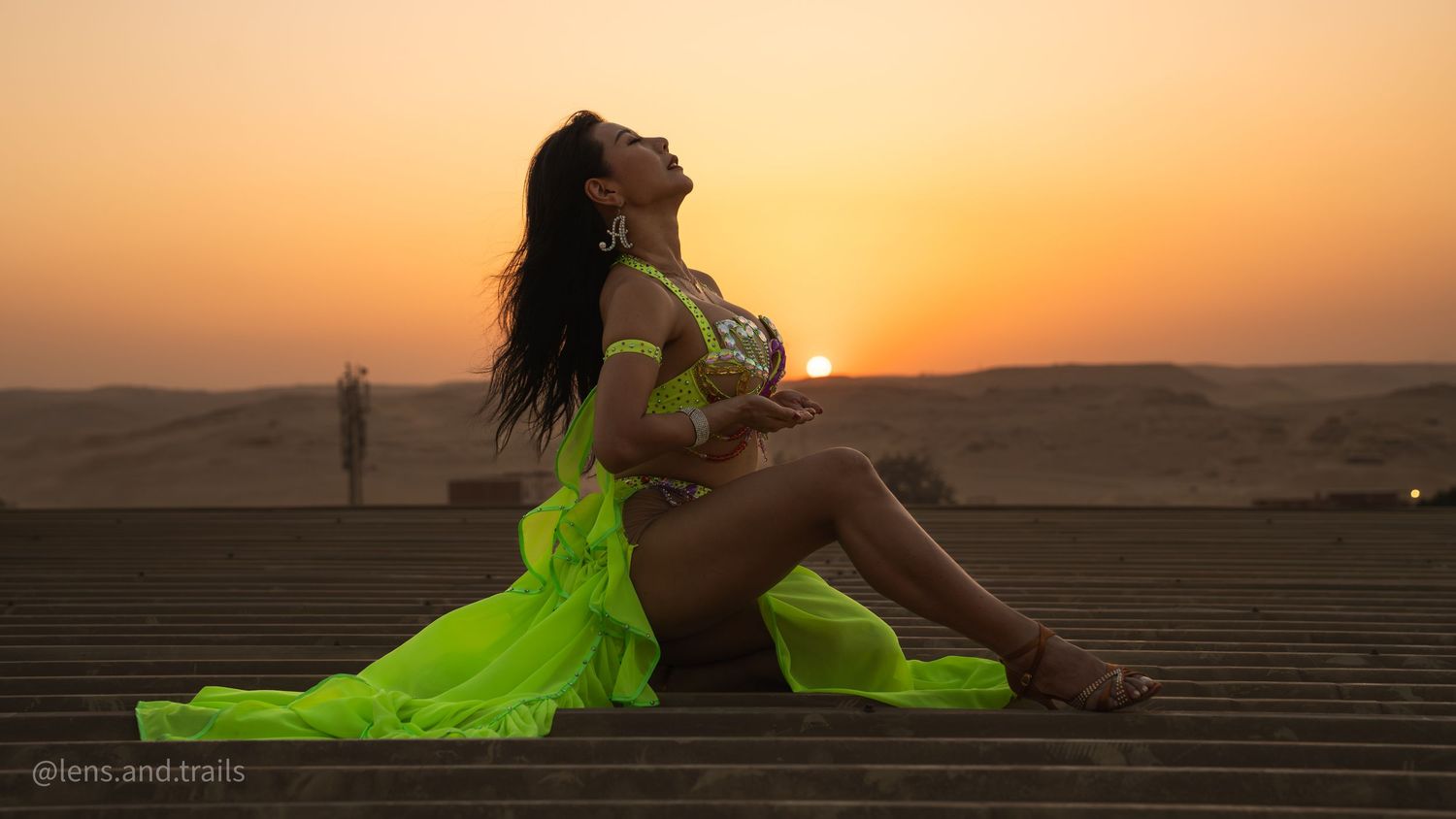 Woman in neon green belly dance costume poses gracefully at sunset in the desert.