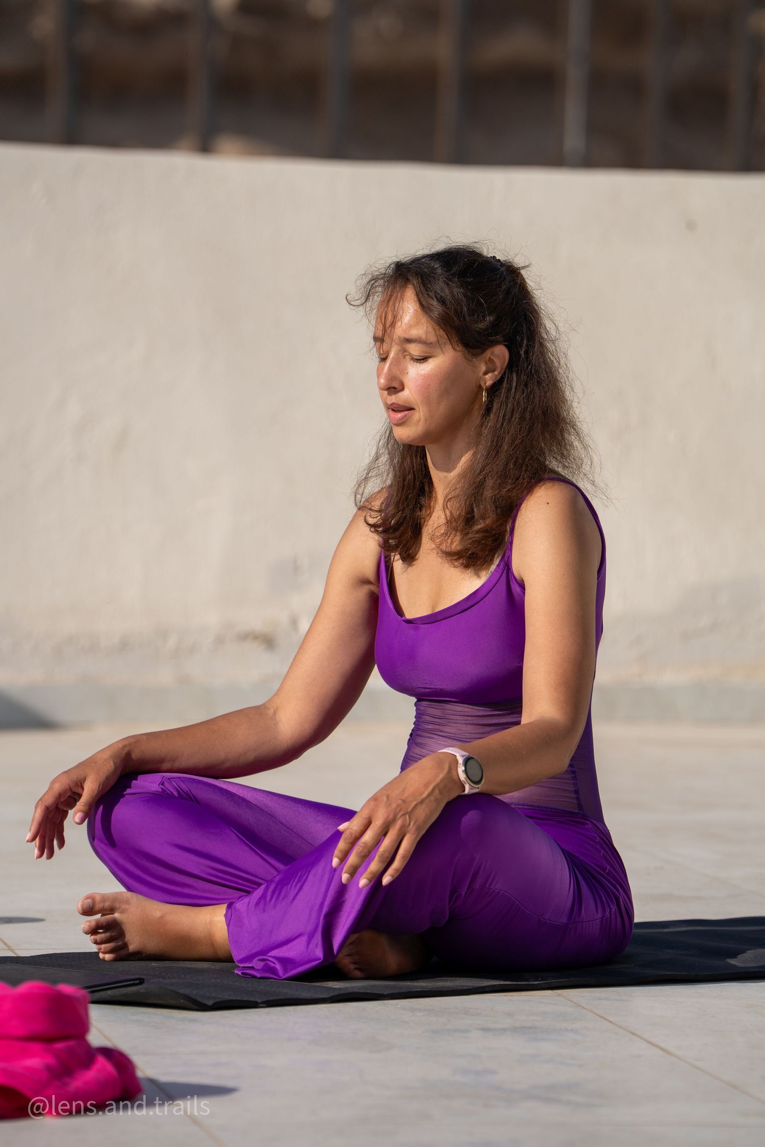Woman in purple yoga outfit meditates in lotus pose on a mat during an outdoor yoga session in Egypt.