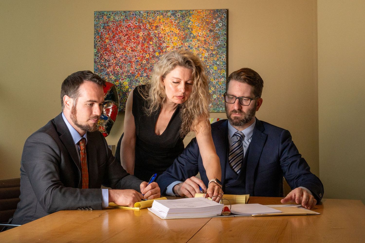 Three colleagues reviewing documents together at a conference table with abstract art in background.