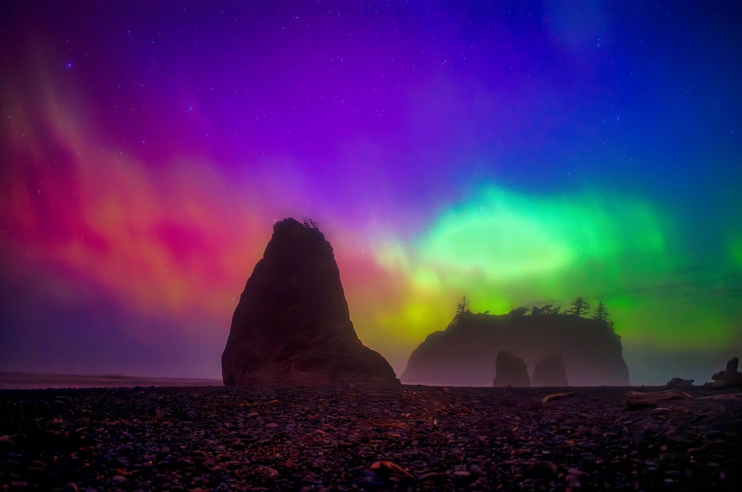 Time-lapse photograph shows colorful aurora borealis lights dancing across a starry night sky over rocky mountain silhouettes.