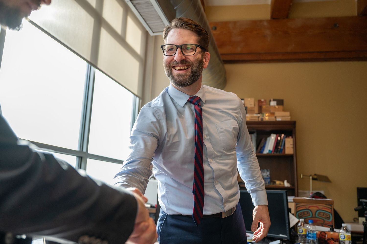 Business professional in business attire greeting someone in a modern office setting.
