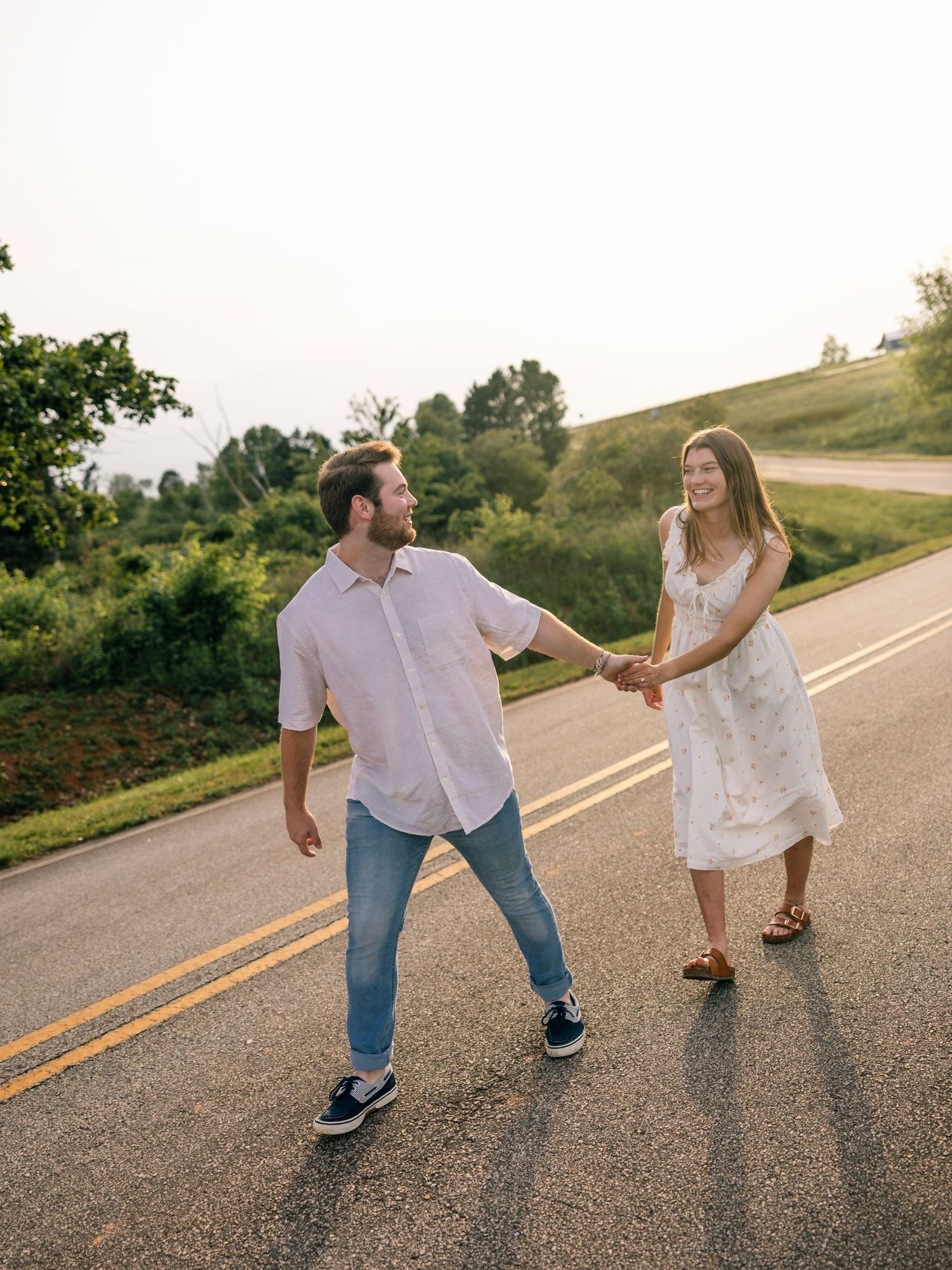 Two people holding hands while strolling down a scenic country road on a sunny afternoon.