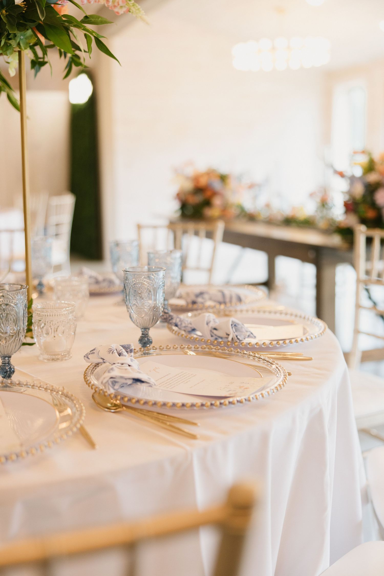 Elegant table settings with white linens, crystal glassware and pearl beaded charger plates in a light-filled reception venue.