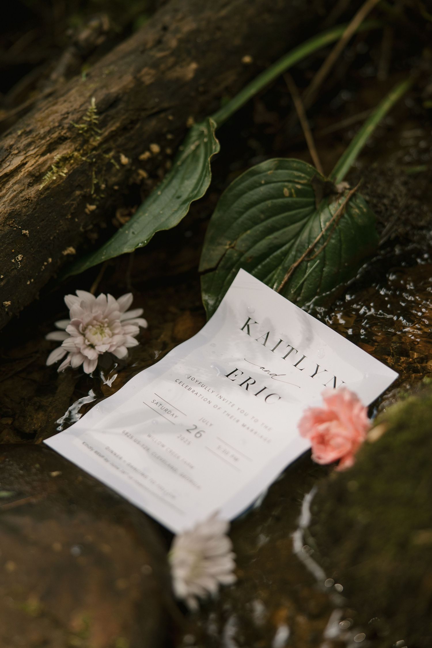 Wedding invitations laid on rustic wooden surface with delicate pink and white flowers as decoration.