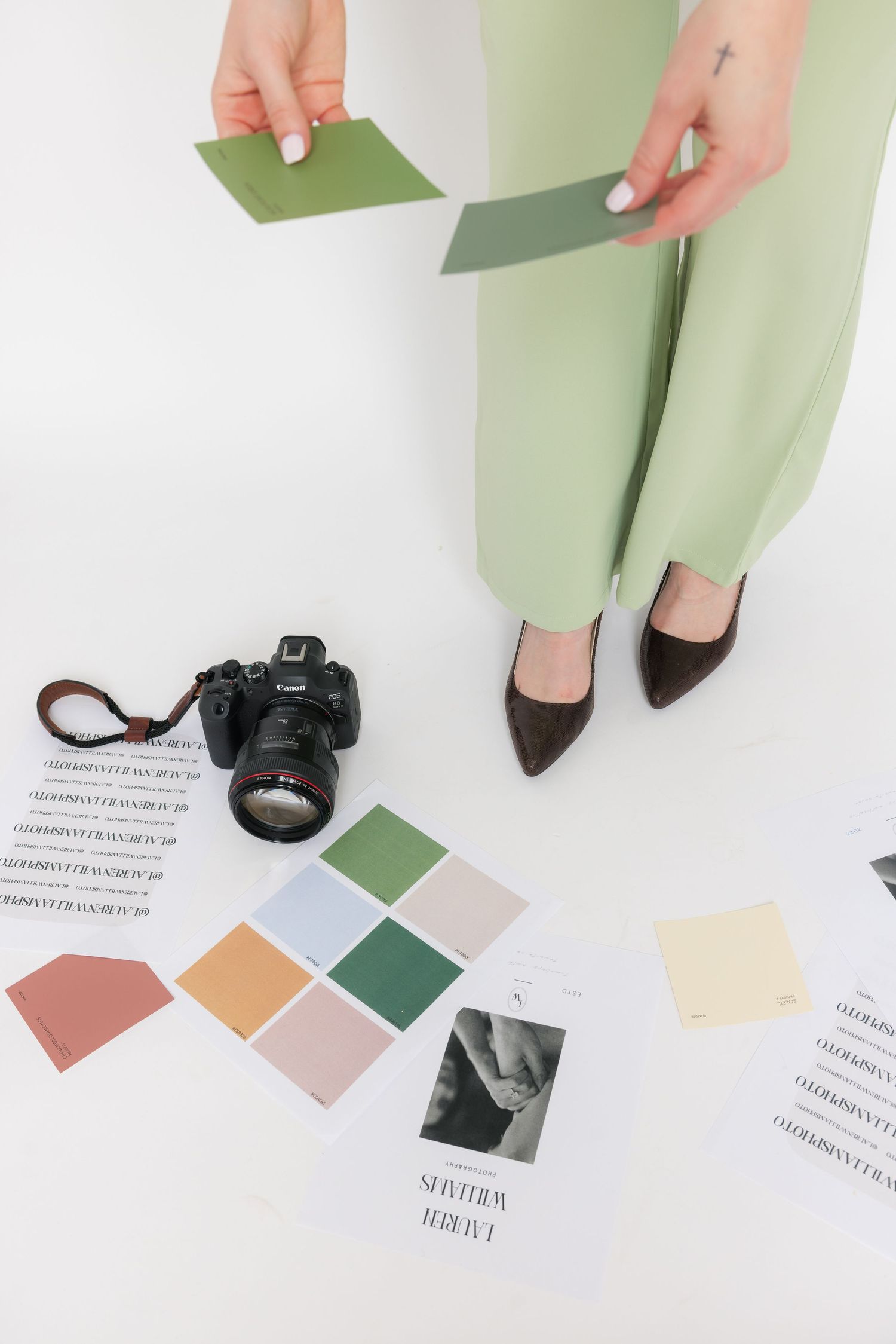 Overhead view of hands holding color swatches with camera and styling elements on white surface.