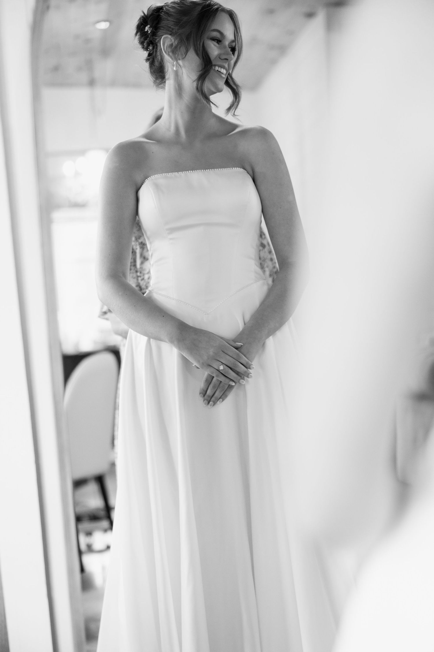 Elegant black and white photograph of a bride wearing a white strapless wedding dress in soft natural light.