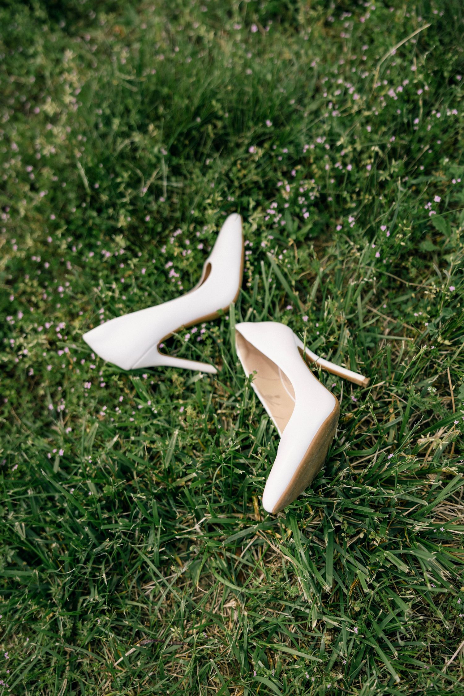 A pair of elegant white stiletto heels sitting on green grass in a garden setting.