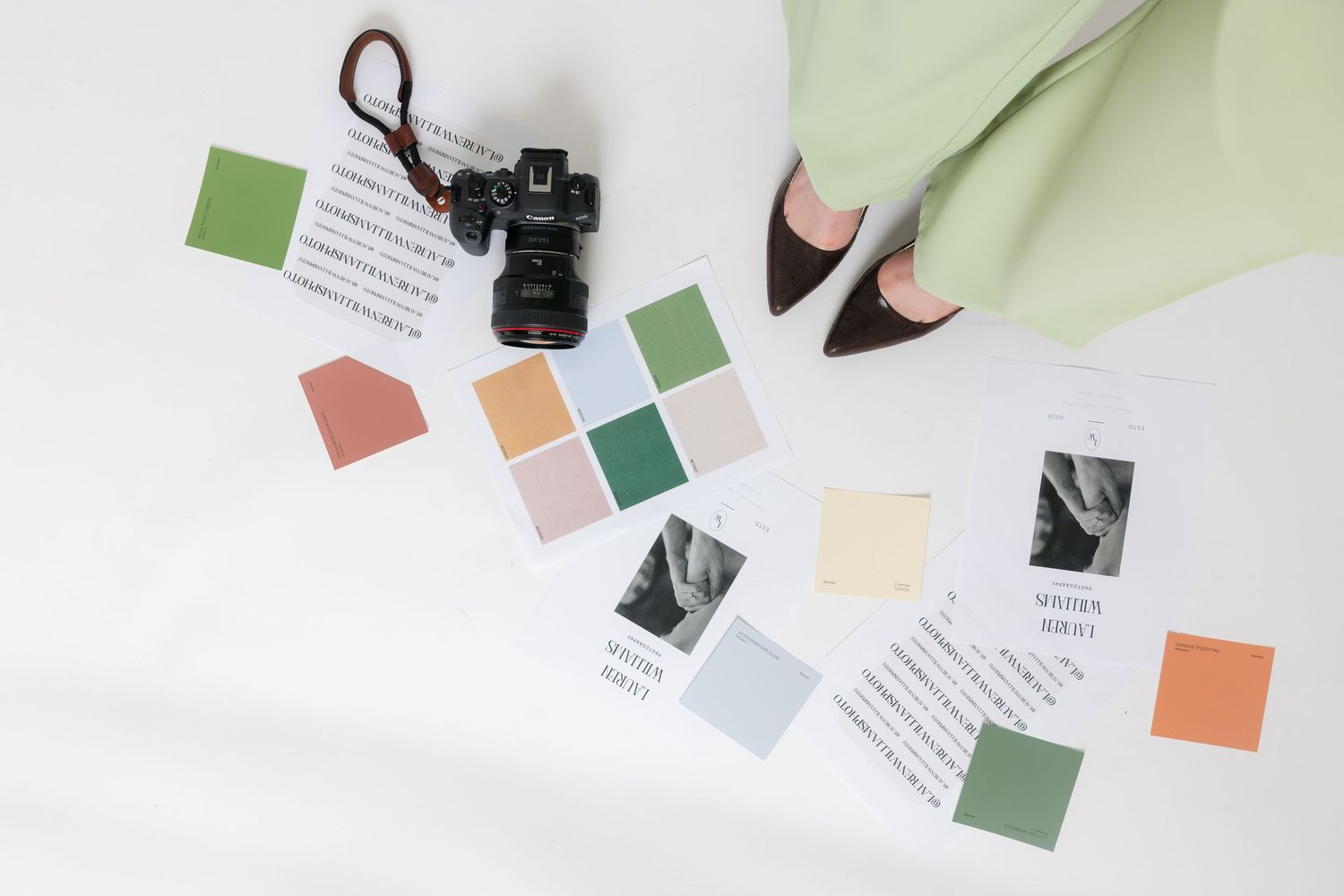 Flatlay of color swatches, notes, and a camera with a pencil on white background.