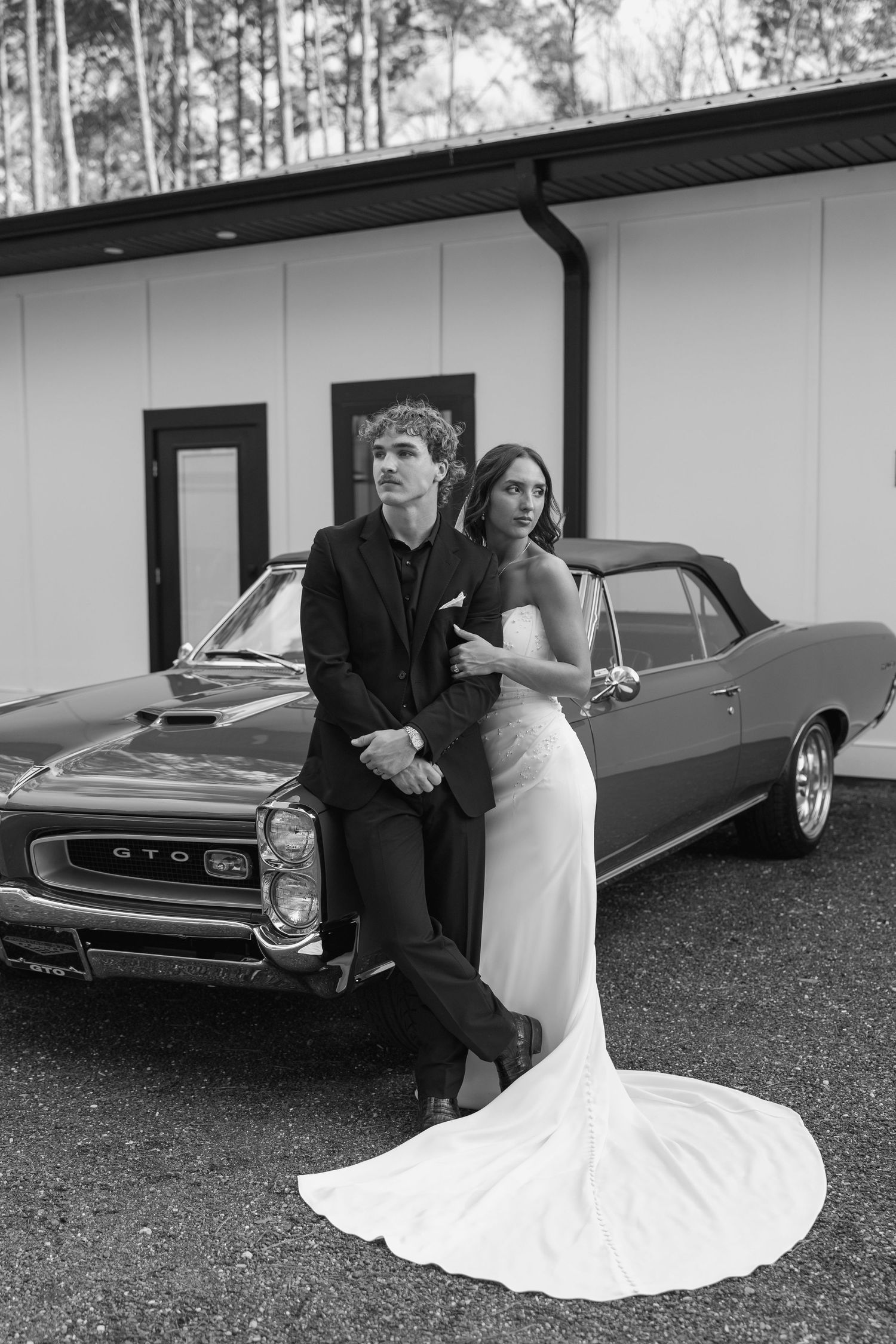 A black and white wedding photo series showing a couple posing with a vintage car, featuring a flowing white bridal gown.