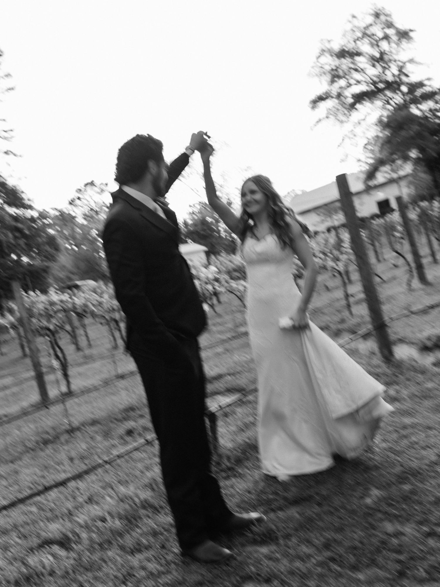 A couple dances together in black and white among vineyard rows on their wedding day.